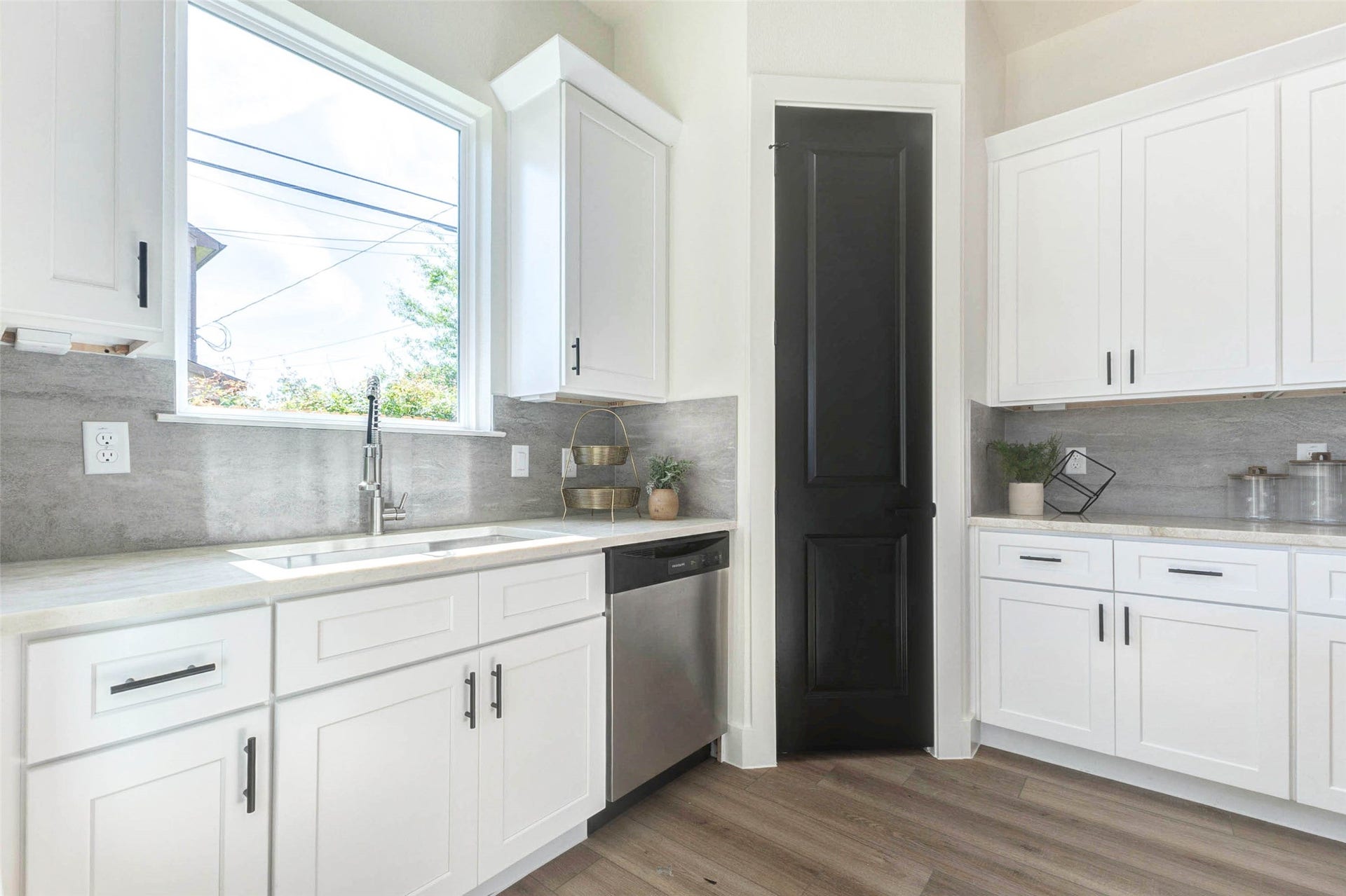 The functional kitchen design includes a deep basin sink, integrated dishwasher, and a contrasting black pantry door.
