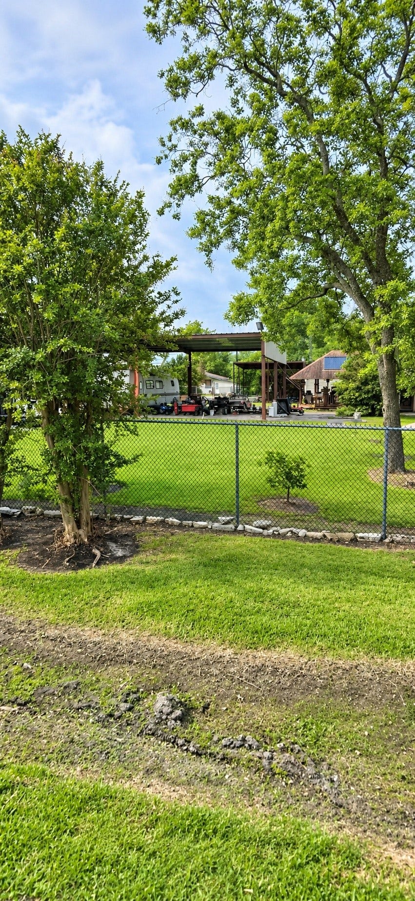 9410 Klondike Street, Houston, TX 77075 View of the property showcasing the chain-link fencing, mature trees, grassy grounds, and existing covered carport structure