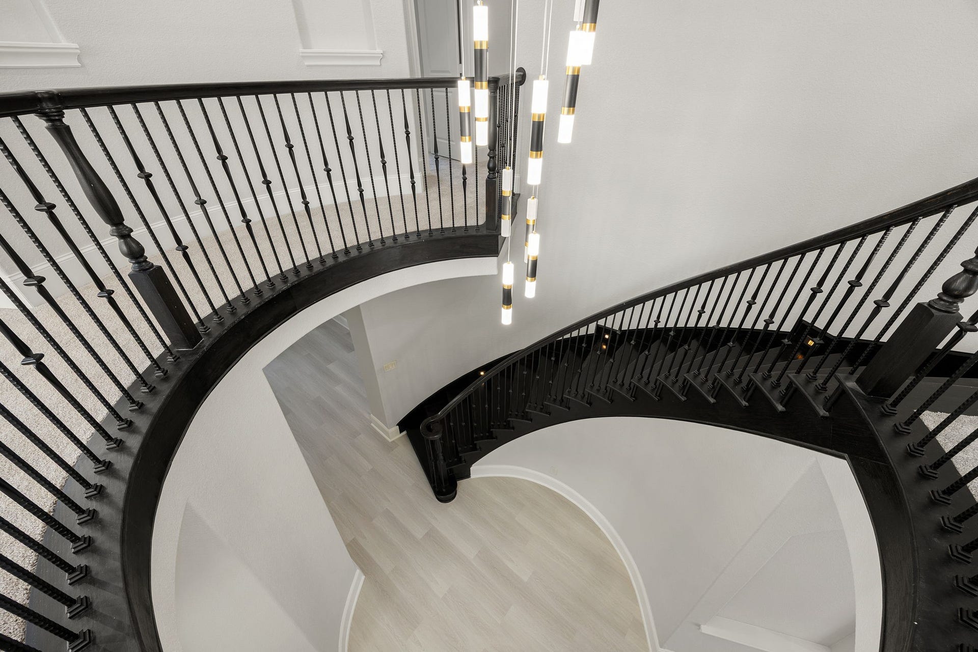 5127 Beekman Drive, Missouri City, TX 77459 Viewed from above, the sweeping curved staircase becomes a sculptural centerpiece, framed by dark wood handrails, black iron balusters, and a cascading modern light fixture.
