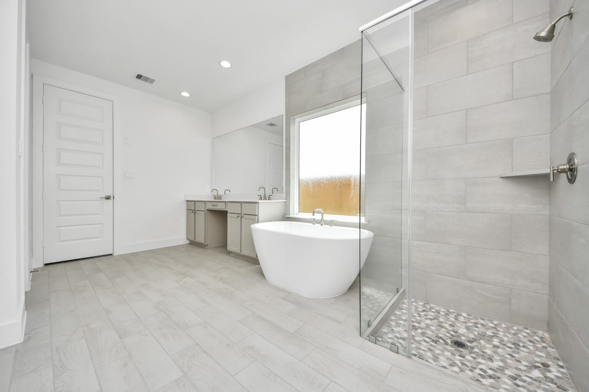 Escape to a spa-like oasis in this primary bathroom. Enjoy a walk-in shower with tile surround, a separate garden tub with custom detailing, and an elegant vanity featuring light countertops, modern hardware, and beautiful recessed lights. Experience luxury and relaxation in every detail. Sample photo of completed home with similar floor plan. Actual colors and selections may vary.