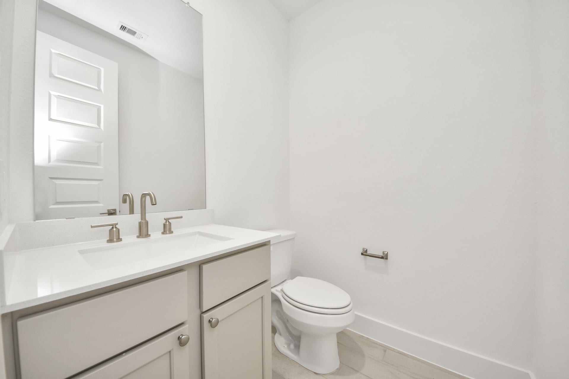 Sophisticated half bathroom adorned with contemporary finishes. The elegant 5-panel door welcomes you to a space where style meets functionality. Notice the sleek hardware accents that add a touch of modern charm. The vanity boasts light-colored countertops, beautifully complemented by a tasteful vanity light, creating a well-lit and inviting atmosphere. Sample photo of completed home with similar floor plan. Actual colors and selections may vary.