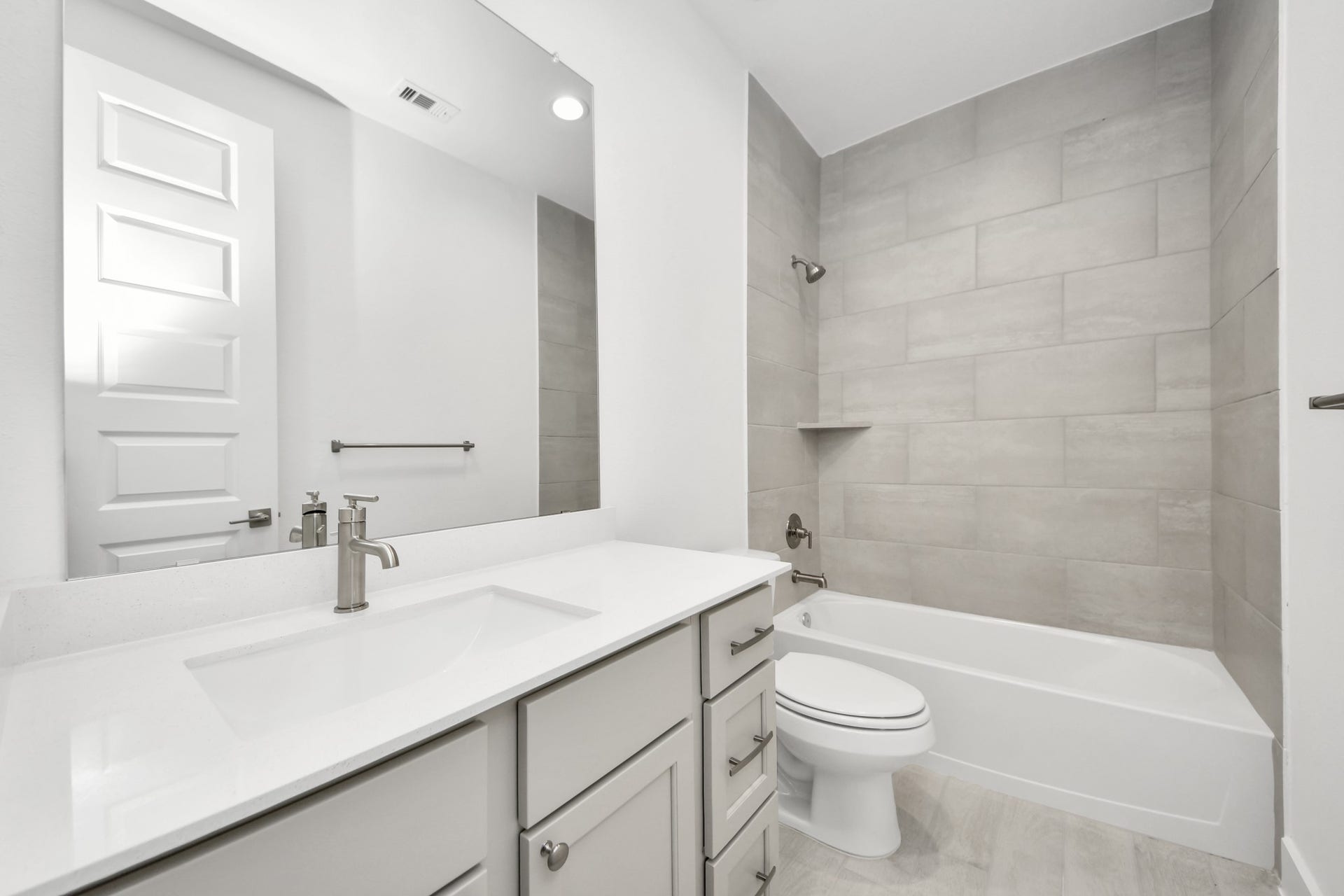 Secondary bath features tile flooring, bath/shower combo with tile surround, light stained wood cabinets, beautiful light countertop. Sample photo of completed home with similar floor plan. Actual colors and selections may vary.