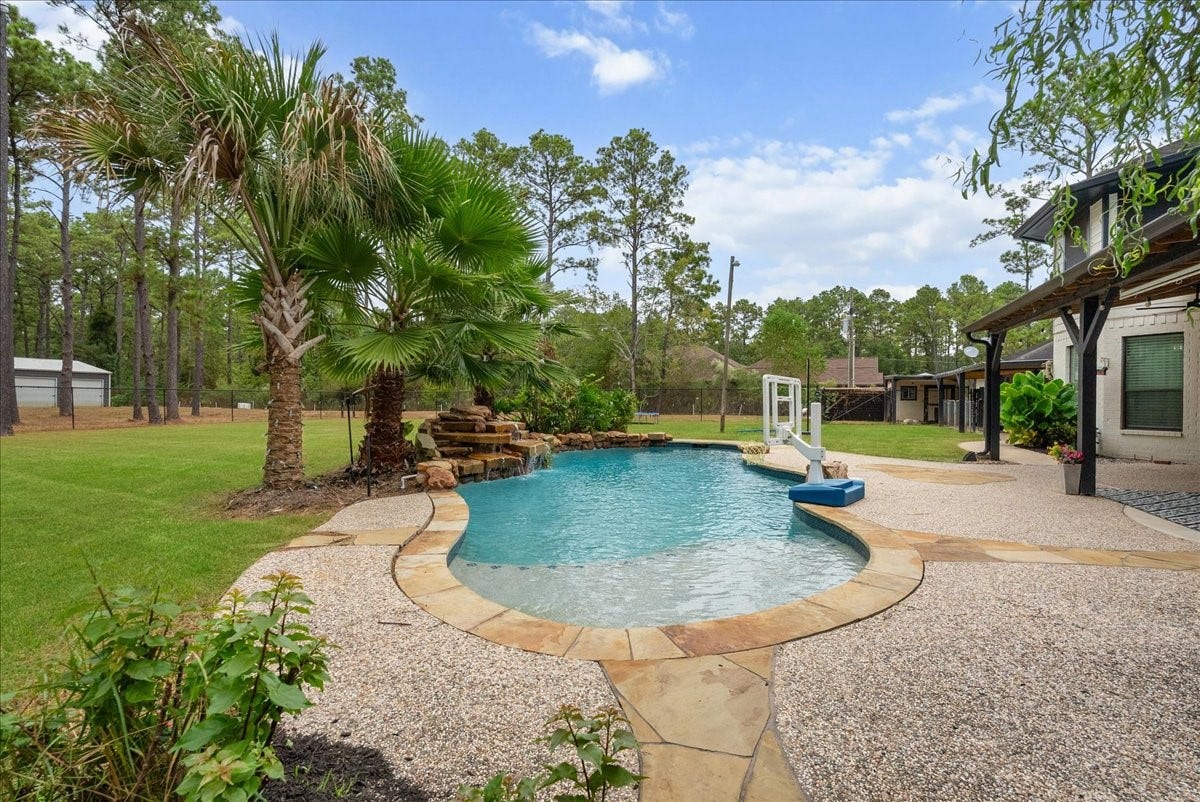 7202 Pine Drive W, Alvin, TX 77511 Experience serene outdoor living with a sparkling pool and waterfall feature, surrounded by lush landscaping and mature trees, perfect for relaxation and entertaining.