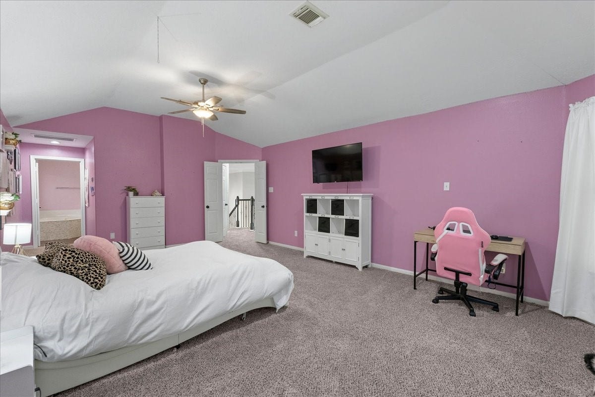 7202 Pine Drive W, Alvin, TX 77511 Spacious upstairs primary bedroom with vibrant pink walls, featuring a cozy bed, modern ceiling fan, and a dedicated workspace with a stylish desk and chair.