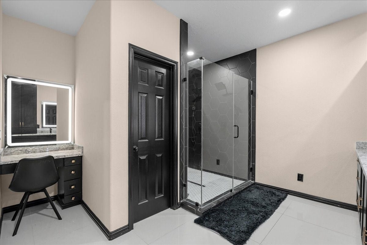 7202 Pine Drive W, Alvin, TX 77511 Elegant primary bathroom featuring a sleek glass-enclosed shower with modern hexagonal tiles and a stylish vanity area complete with a backlit mirror.