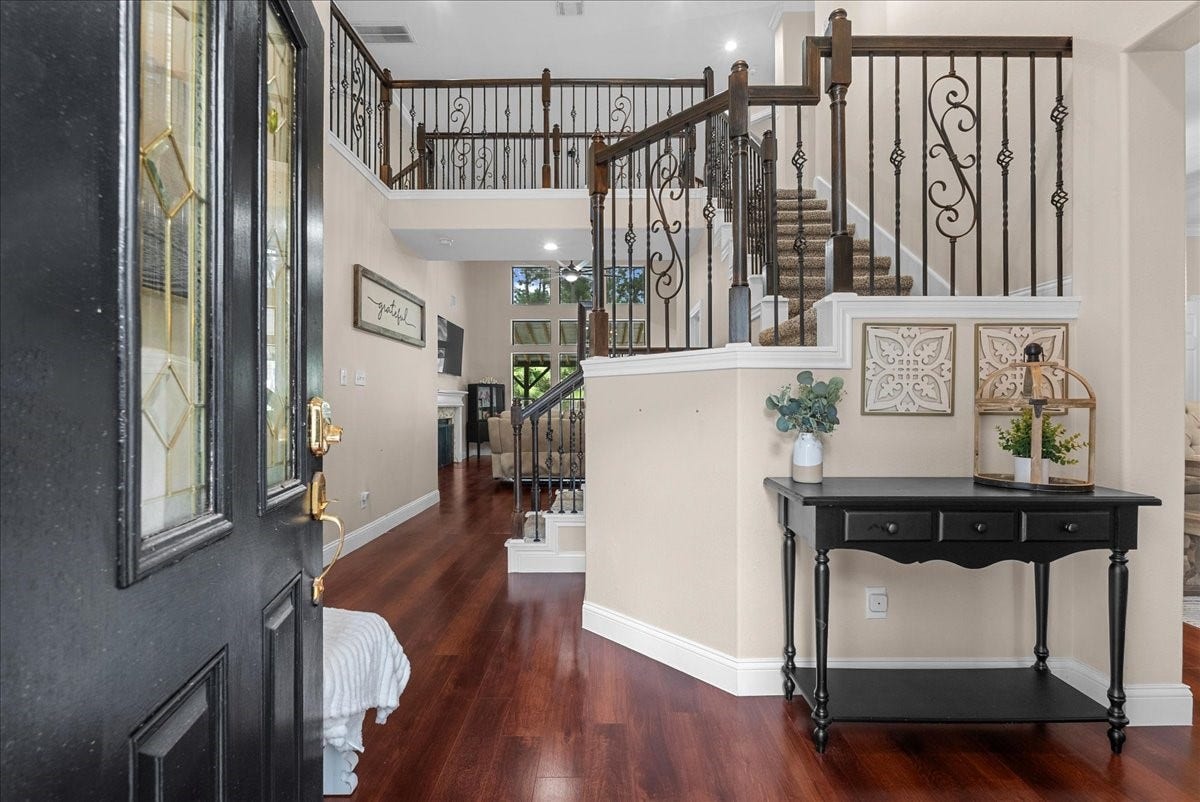 7202 Pine Drive W, Alvin, TX 77511 Elegant entryway featuring rich hardwood like floors and a charming staircase with decorative wrought iron railings, leading to a spacious and inviting living area.