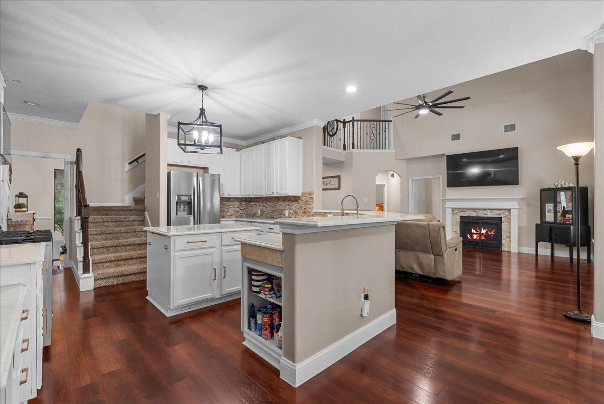 7202 Pine Drive W, Alvin, TX 77511 Spacious open-concept living area featuring a modern kitchen with stainless steel appliances, elegant cabinetry, and a large island. The cozy living room boasts a stylish fireplace and high ceilings, enhanced by natural light and wood like flooring.