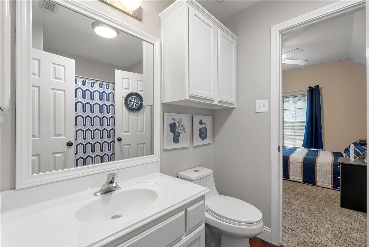 7202 Pine Drive W, Alvin, TX 77511 Bright bathroom with modern fixtures, ample storage, and a stylish blue geometric shower curtain, leading into a cozy bedroom with natural light.