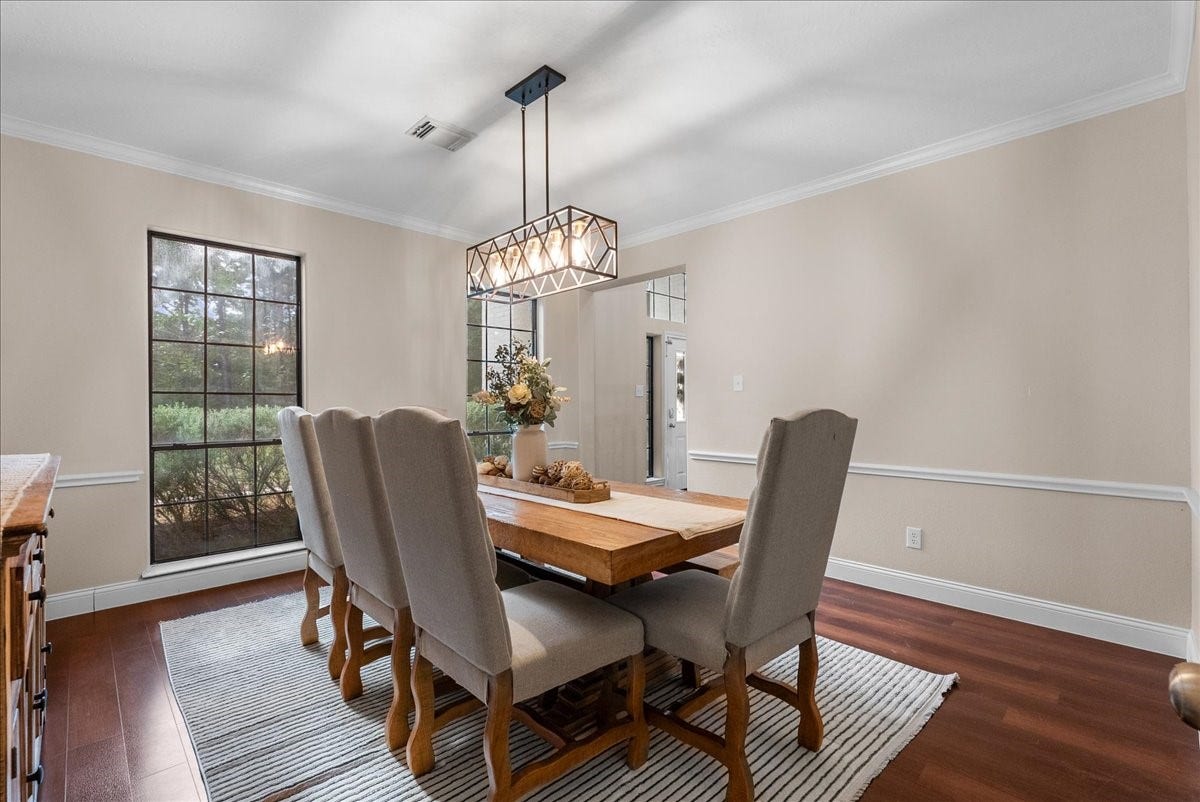 7202 Pine Drive W, Alvin, TX 77511 Elegant dining room with rich wood like floring, a large window offering natural light, and a stylish chandelier above a spacious table, perfect for gatherings.
