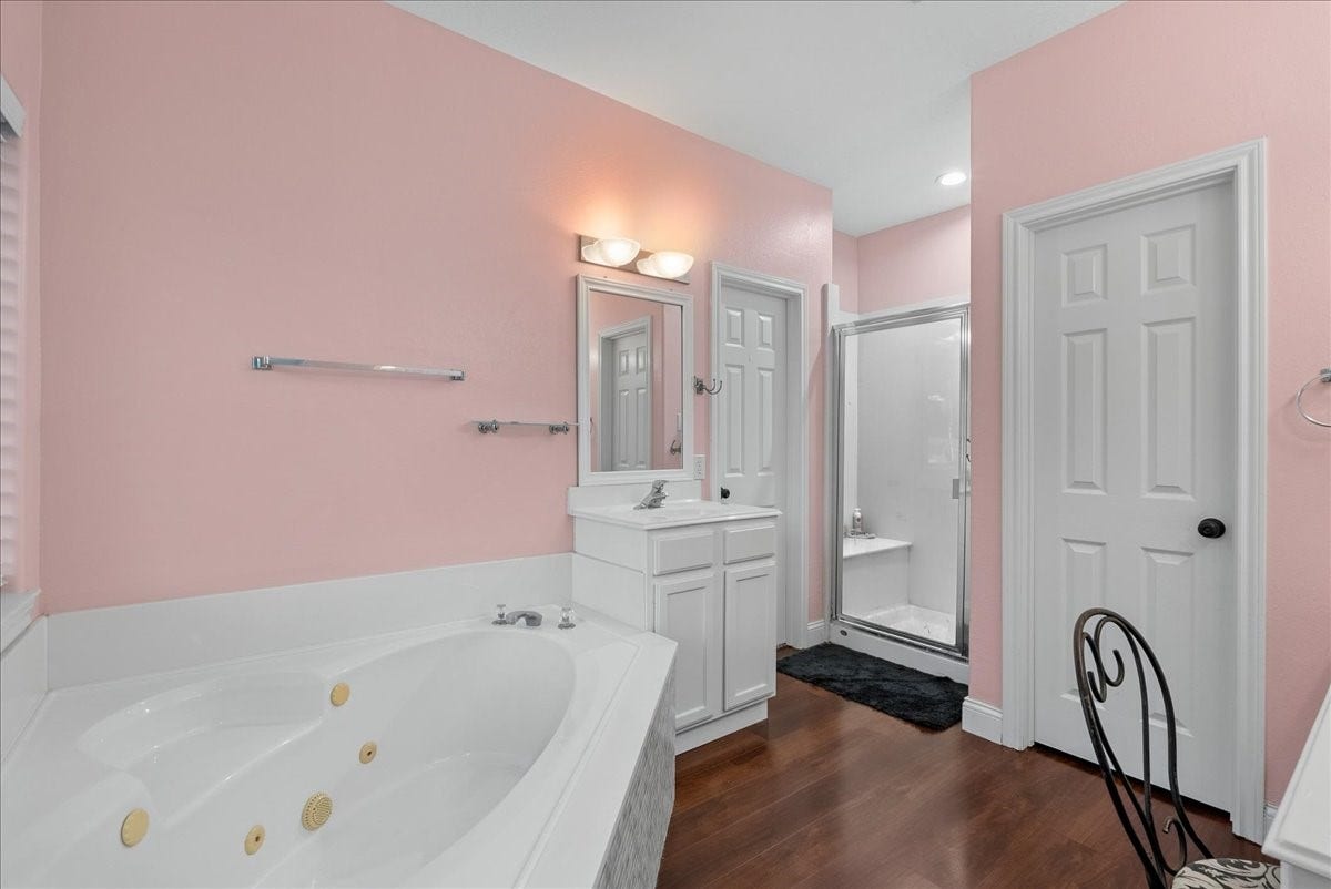 7202 Pine Drive W, Alvin, TX 77511 Charming bathroom with soft pink walls, featuring a luxurious jetted tub, a sleek walk-in shower, and elegant wood like flooring.