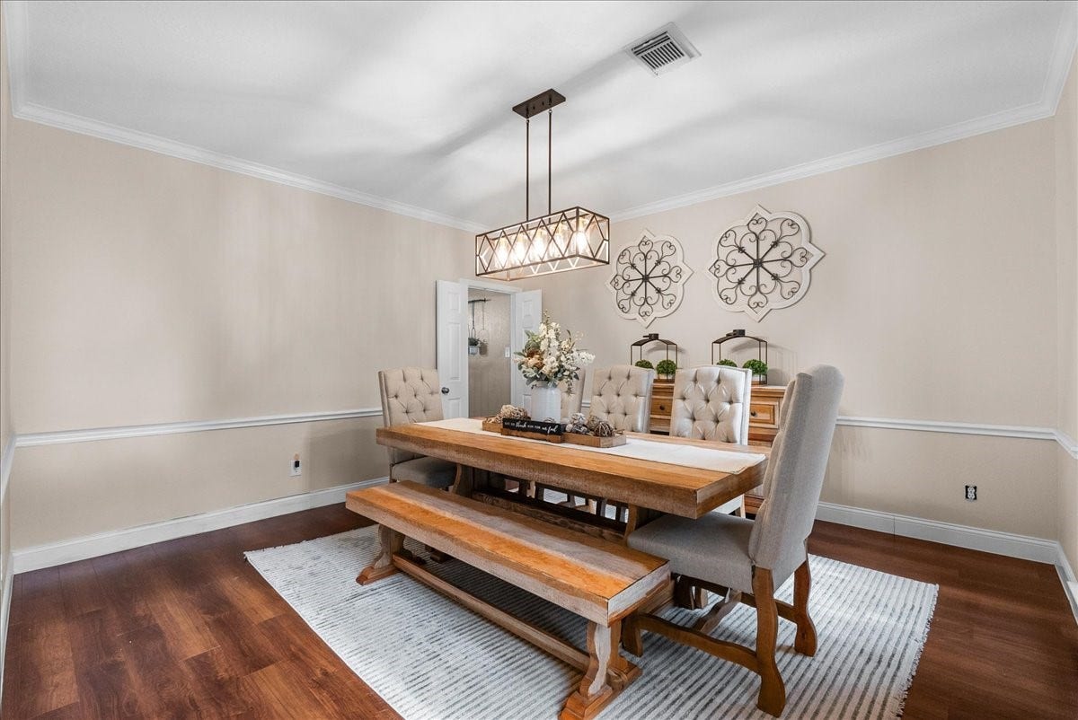 7202 Pine Drive W, Alvin, TX 77511 Elegant dining room featuring a rustic wooden table with bench seating, plush upholstered chairs, and a stylish chandelier, set against warm-toned walls and chic decor accents.