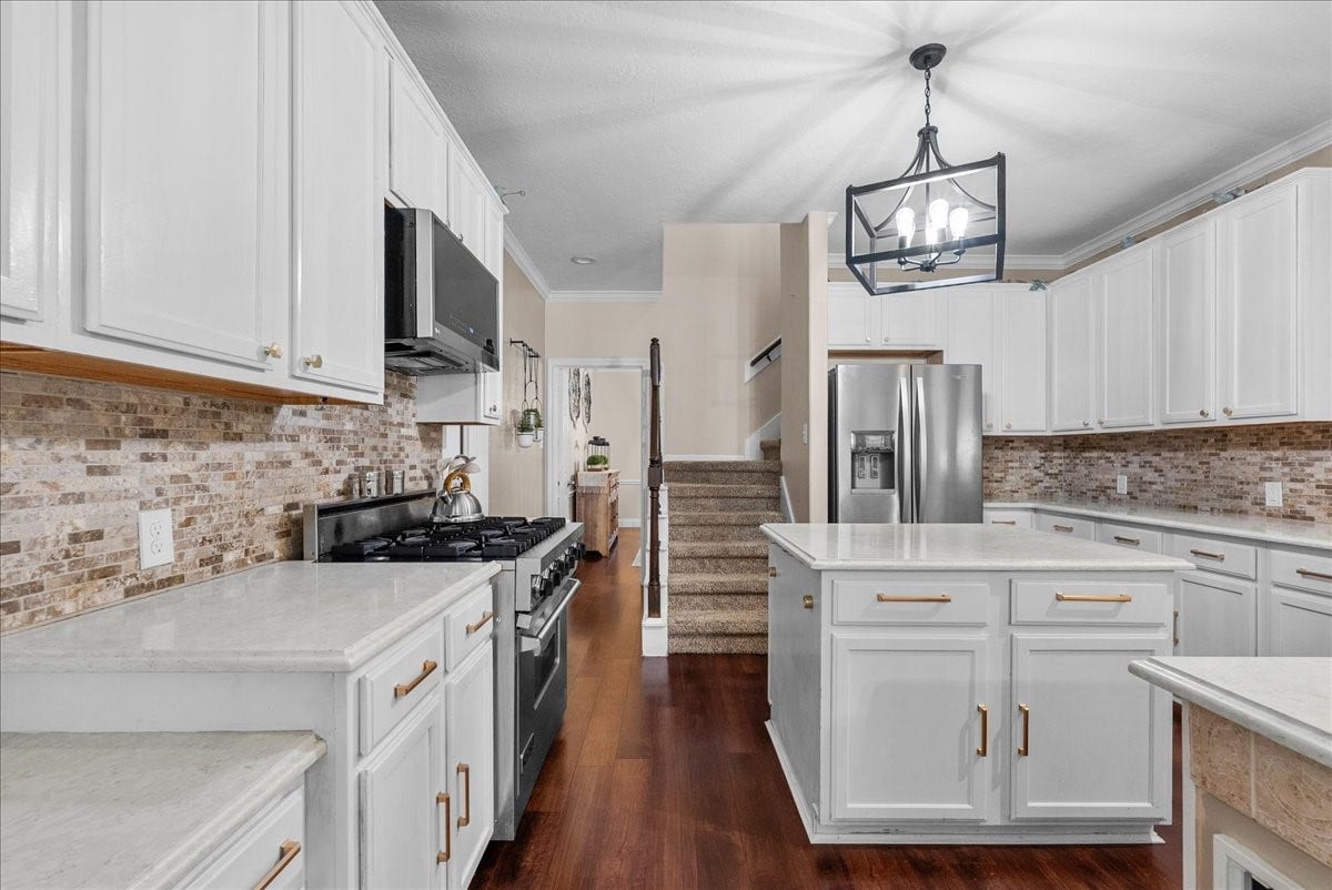 7202 Pine Drive W, Alvin, TX 77511 Spacious kitchen featuring elegant white cabinetry, sleek stainless steel appliances, and a charming brick backsplash, complemented by rich wood like flooring and a stylish central island.