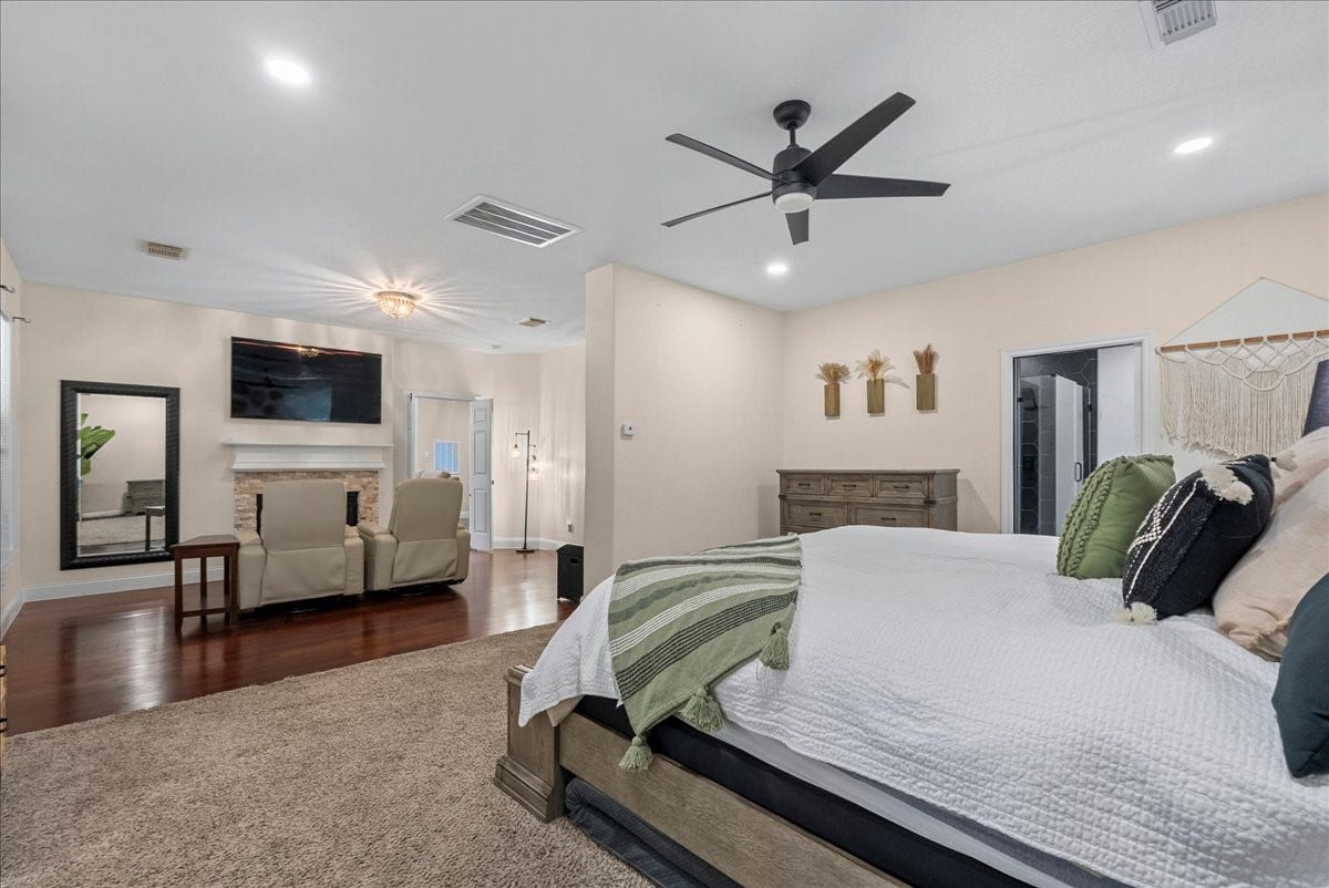 7202 Pine Drive W, Alvin, TX 77511 Spacious primary bedroom featuring elegant hardwood like floors, a cozy seating area by the fireplace, and modern ceiling fan, creating a luxurious retreat.
