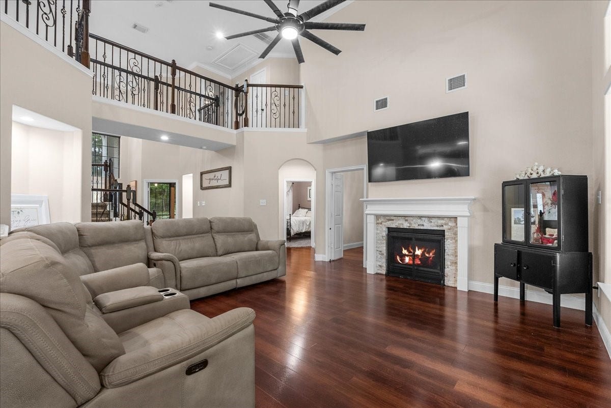 7202 Pine Drive W, Alvin, TX 77511 Spacious living room featuring high ceilings, a cozy fireplace, and a modern staircase, complemented by elegant wood like flooring and a abundance of natural light.