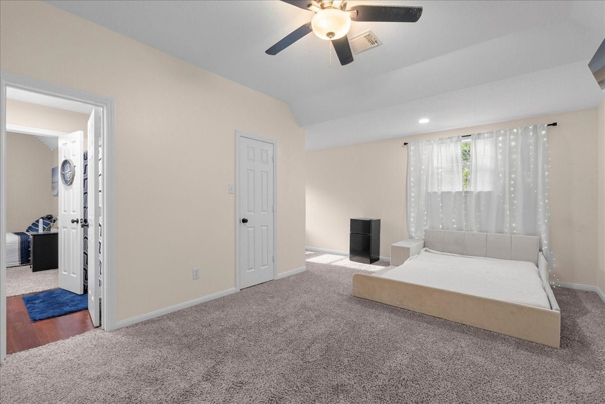 7202 Pine Drive W, Alvin, TX 77511 Spacious bedroom with soft carpeting, featuring a ceiling fan and ample natural light from a large window, complemented by a modern bed and neutral decor.