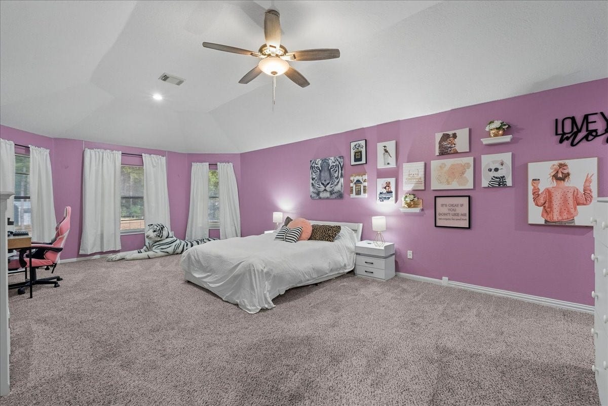 7202 Pine Drive W, Alvin, TX 77511 Spacious upstairs primary bedroom with vibrant pink walls, cozy carpeting, and a stylish gallery wall, featuring a comfortable bed and ample natural light.