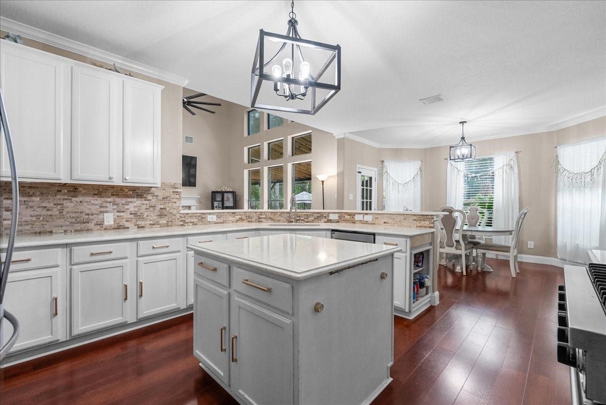 7202 Pine Drive W, Alvin, TX 77511 Bright and inviting kitchen features elegant white cabinetry, a spacious island with modern lighting fixtures, and an open layout leading to a cozy dining area with large windows.