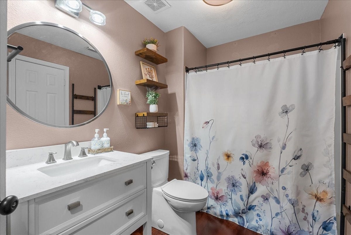 7202 Pine Drive W, Alvin, TX 77511 Charming bathroom featuring a stylish round mirror, elegant vanity, and a floral shower curtain that adds a touch of color and warmth.