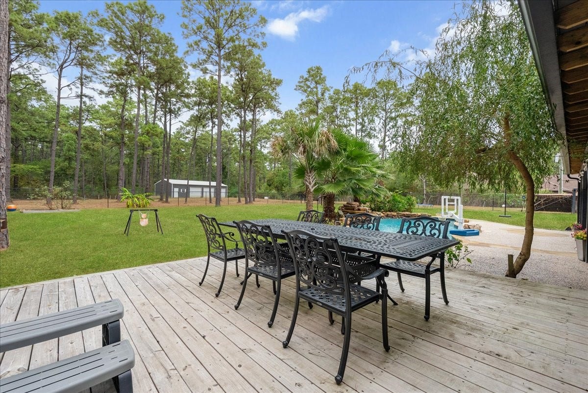 7202 Pine Drive W, Alvin, TX 77511 Expansive backyard retreat featuring a spacious deck with elegant wrought iron furniture, a lush lawn, and a sparkling pool surrounded by mature trees for added privacy and tranquility.