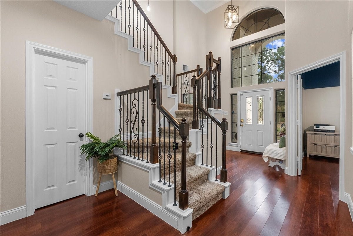 7202 Pine Drive W, Alvin, TX 77511 Elegant foyer with a grand staircase, featuring wrought iron railings and rich hardwood like floors, complemented by high ceilings and a large arched window for natural light.