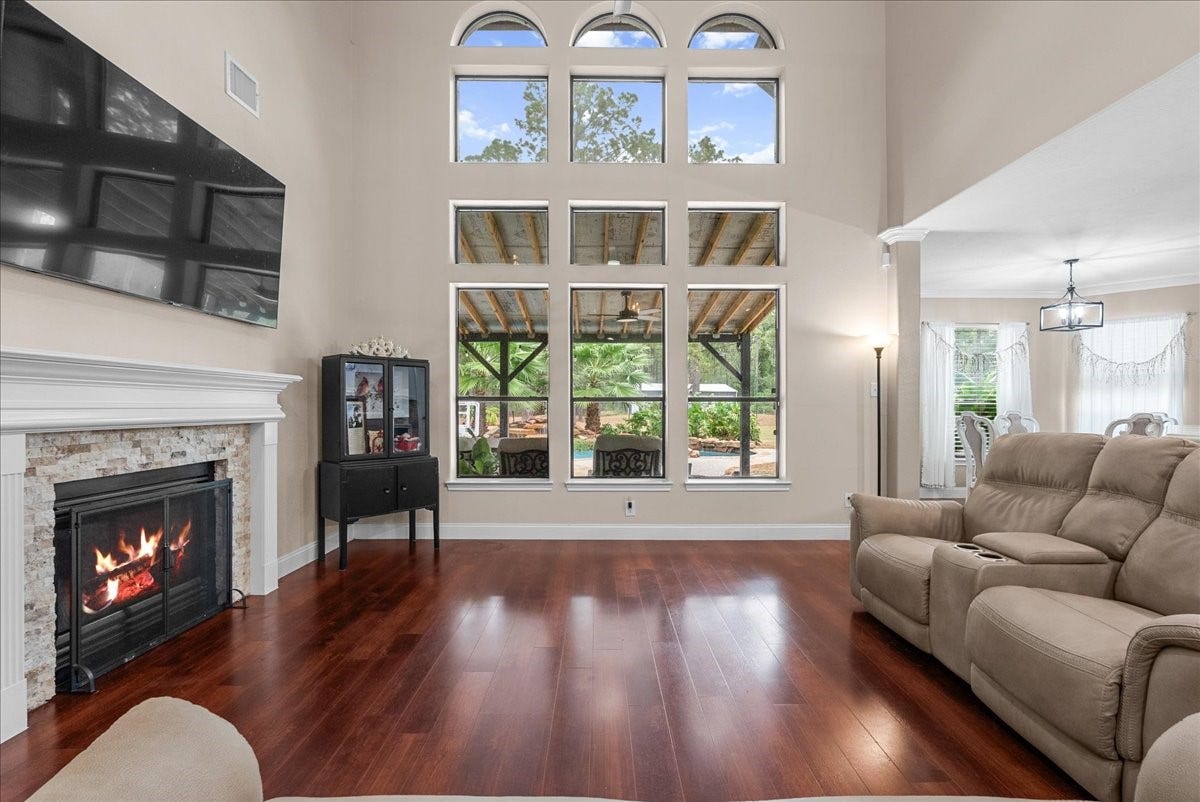 7202 Pine Drive W, Alvin, TX 77511 Stunning living room with soaring ceilings and expansive windows, featuring a cozy fireplace and elegant hardwood like floors, seamlessly flowing into the dining area for a perfect blend of comfort and style.