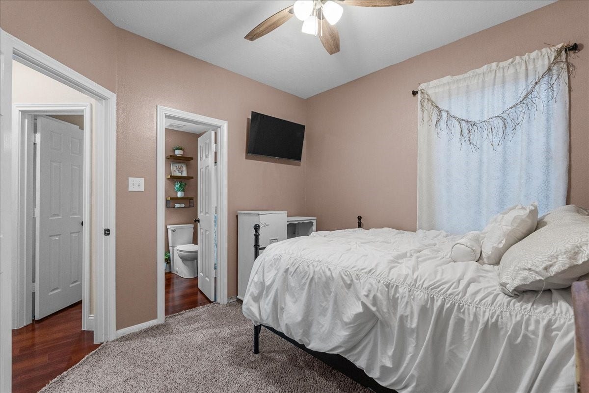 7202 Pine Drive W, Alvin, TX 77511 Cozy bedroom with warm tones features a plush carpet, ceiling fan, and wall-mounted TV, seamlessly connected to an ensuite bathroom for added convenience.