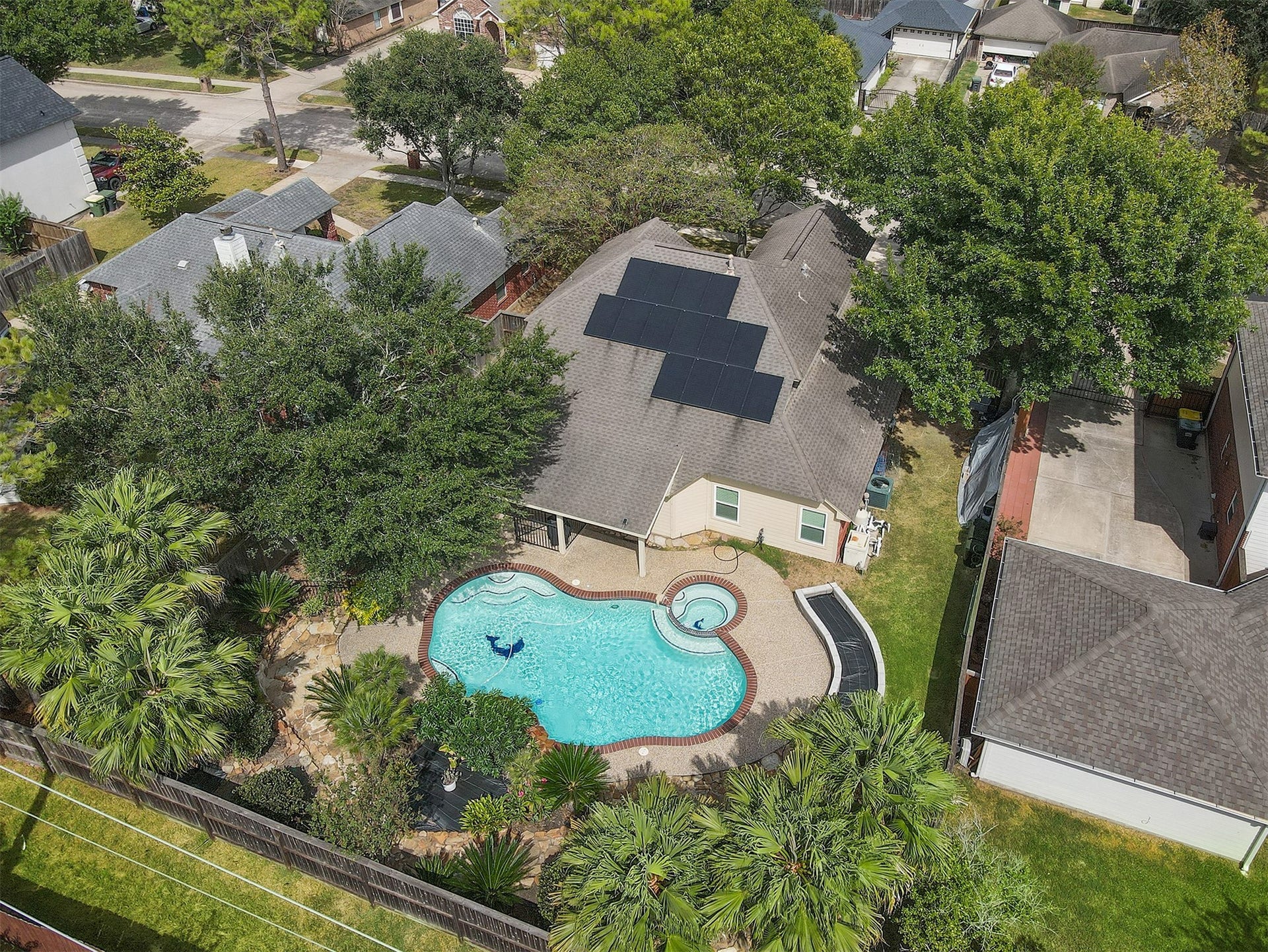 3424 Glastonbury Drive, Pearland, TX 77581 This charming home features a spacious backyard with a beautiful swimming pool and spa, surrounded by lush greenery and mature trees, offering a private oasis for relaxation and entertainment. Solar panels adorn the roof, enhancing energy efficiency.