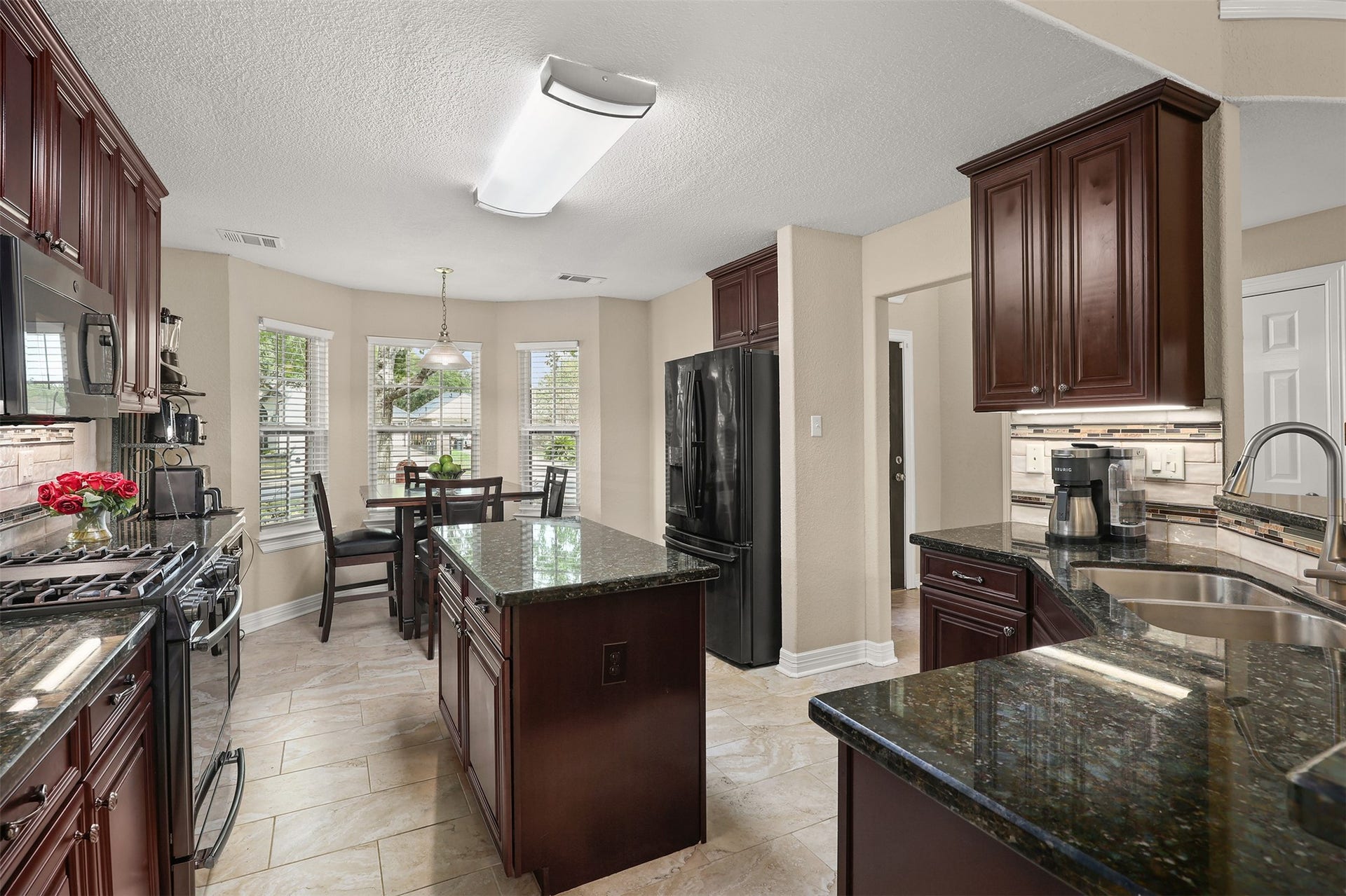3424 Glastonbury Drive, Pearland, TX 77581 Charming kitchen with wood cabinetry, granite countertops, and modern appliances. The bright breakfast nook offers a dining space and breakfast bar with abundant natural light.