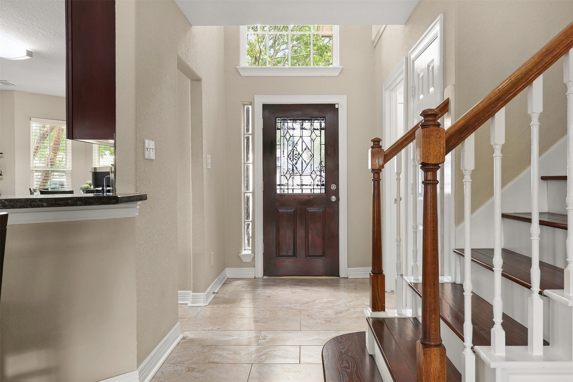 3424 Glastonbury Drive, Pearland, TX 77581 Elegant entryway featuring a decorative glass front door, rich wood staircase with white balusters, and tiled flooring leading to an open kitchen area.