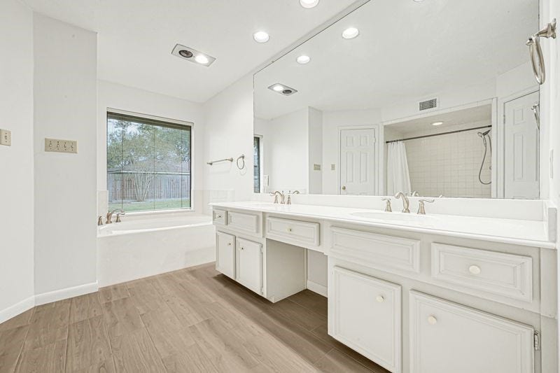 9907 Sagegreen Drive, Houston, TX 77089 Bathroom features a spacious double vanity with elegant fixtures, a large mirror, and a relaxing soaking tub by the window, all accentuated by stylish wood flooring.