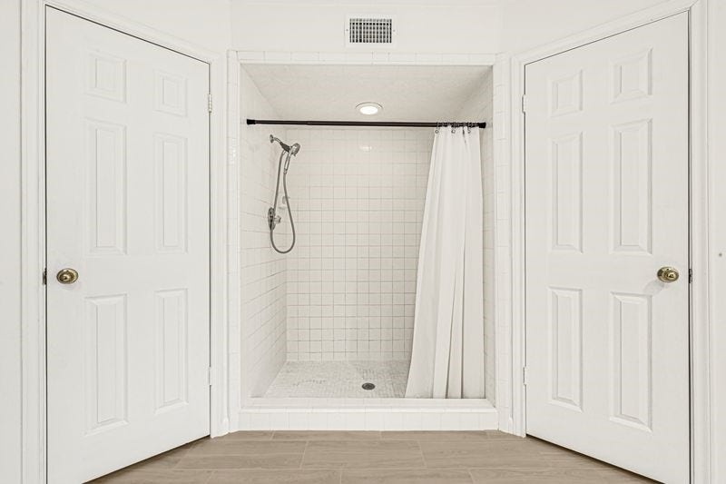 9907 Sagegreen Drive, Houston, TX 77089 Spacious walk-in shower with sleek white tiles and a convenient handheld showerhead, flanked by double doors for easy access.
