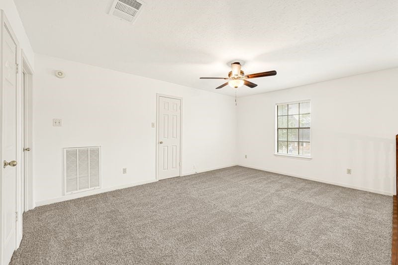 9907 Sagegreen Drive, Houston, TX 77089 Spacious room with plush carpeting, a ceiling fan, and abundant natural light from a large window, perfect for relaxation.