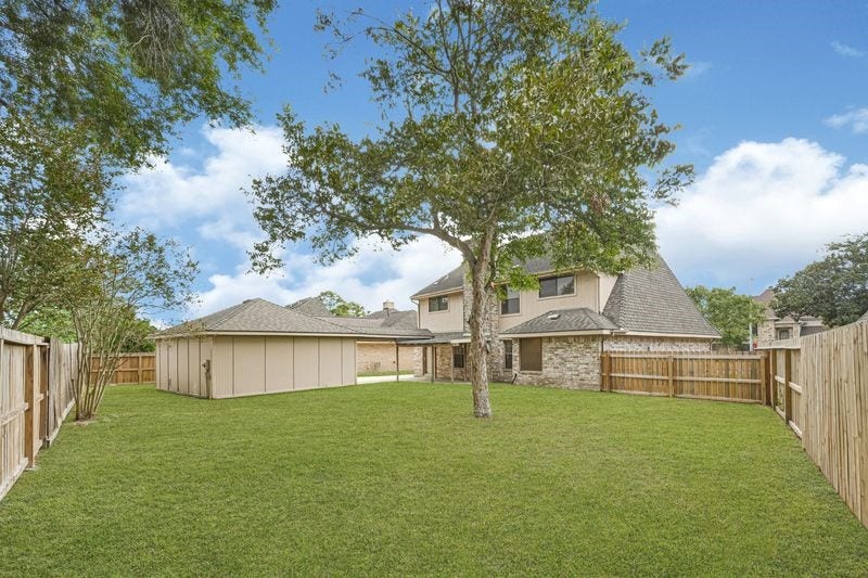 9907 Sagegreen Drive, Houston, TX 77089 Spacious backyard with lush green lawn, mature trees, and a privacy fence, perfect for outdoor activities and relaxation.