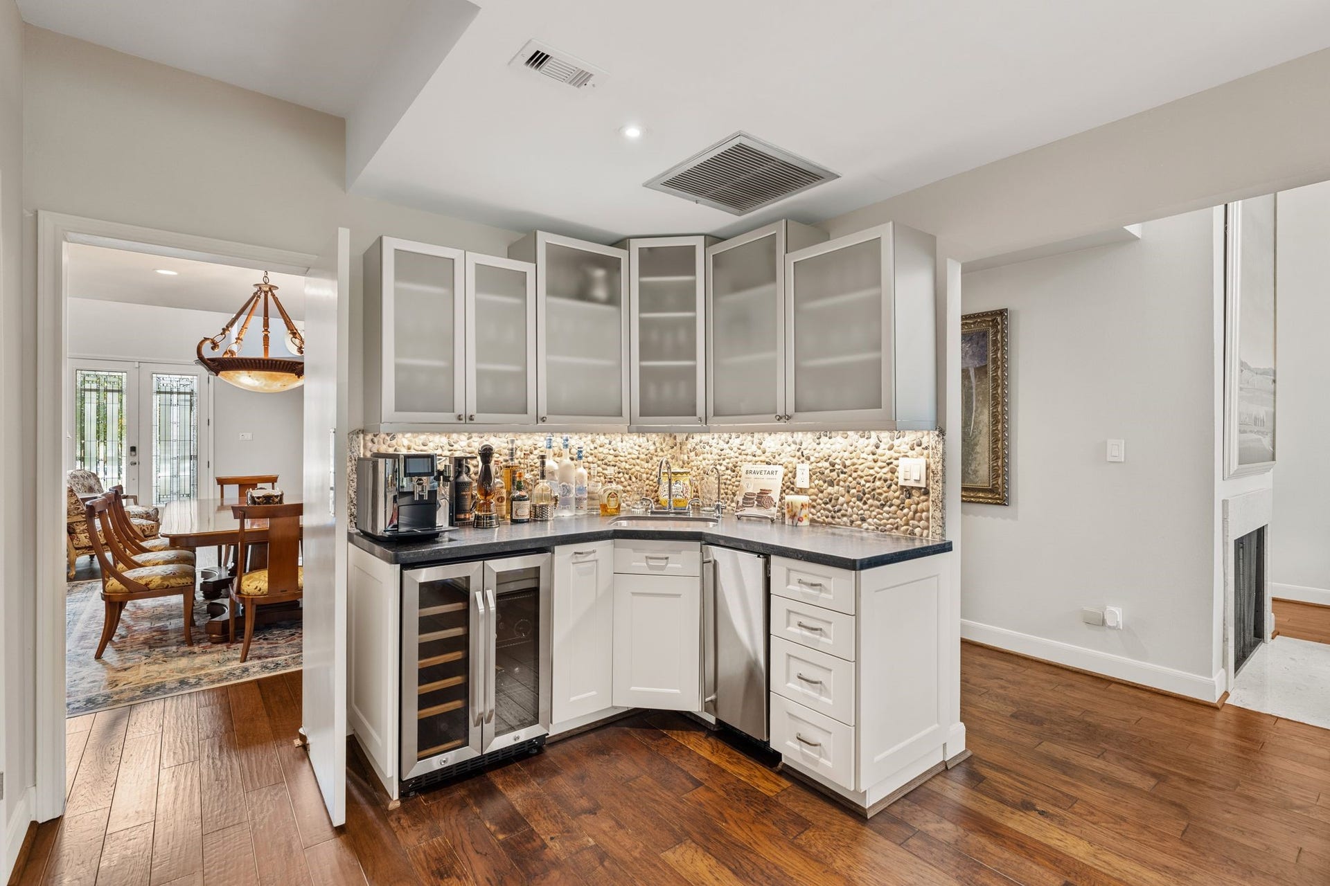 1918 Stoney Brook Drive, Houston, TX 77063 The wet bar with a sink, beverage refrigerator, illuminated pebble backsplash and glass-front cabinetry is perfectly located between the dining room and kitchen.