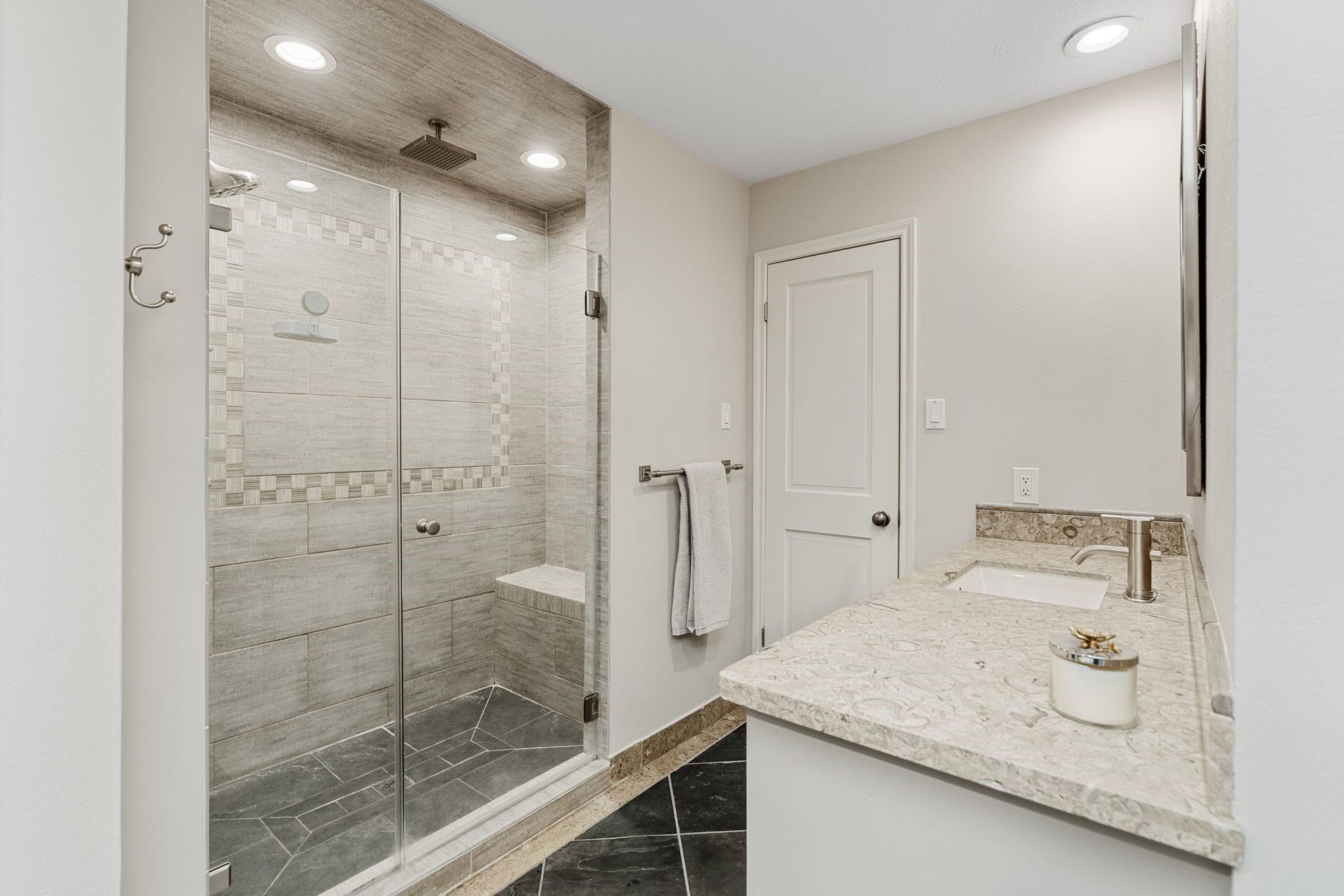 1918 Stoney Brook Drive, Houston, TX 77063 The primary bath features a spacious glass-enclosed shower with a rainfall showerhead, built-in bench and decorative tile accents.