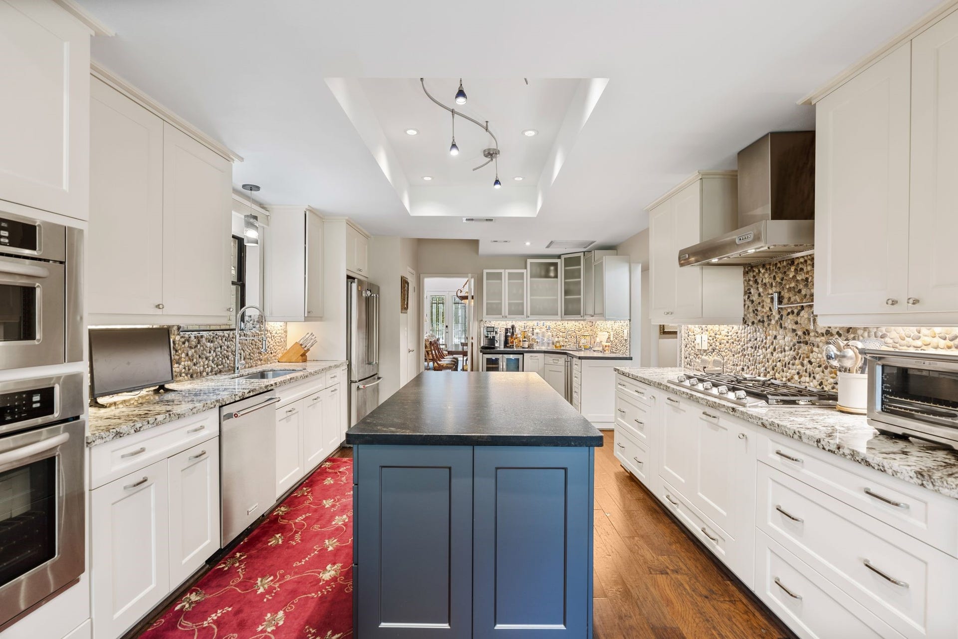 1918 Stoney Brook Drive, Houston, TX 77063 The kitchen features a contrasting blue island, granite countertops, gas cooking and a distinctive pebble backsplash, complemented by abundant white cabinetry.