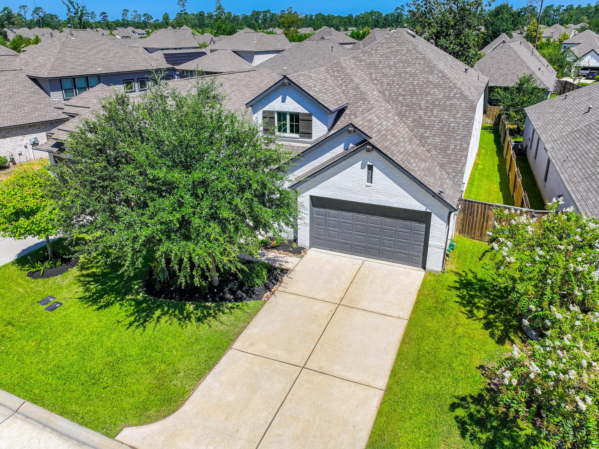 706 Santa Elena Trail, Conroe, TX 77304 Bird's-eye aerial view of 706 Santa Elena Trail shows the home's generous lot, manicured green yard, two-car garage, and ideal location within Grand Central Park. The neighborhood's lush tree canopy and master-planned layout are clearly visible from above.