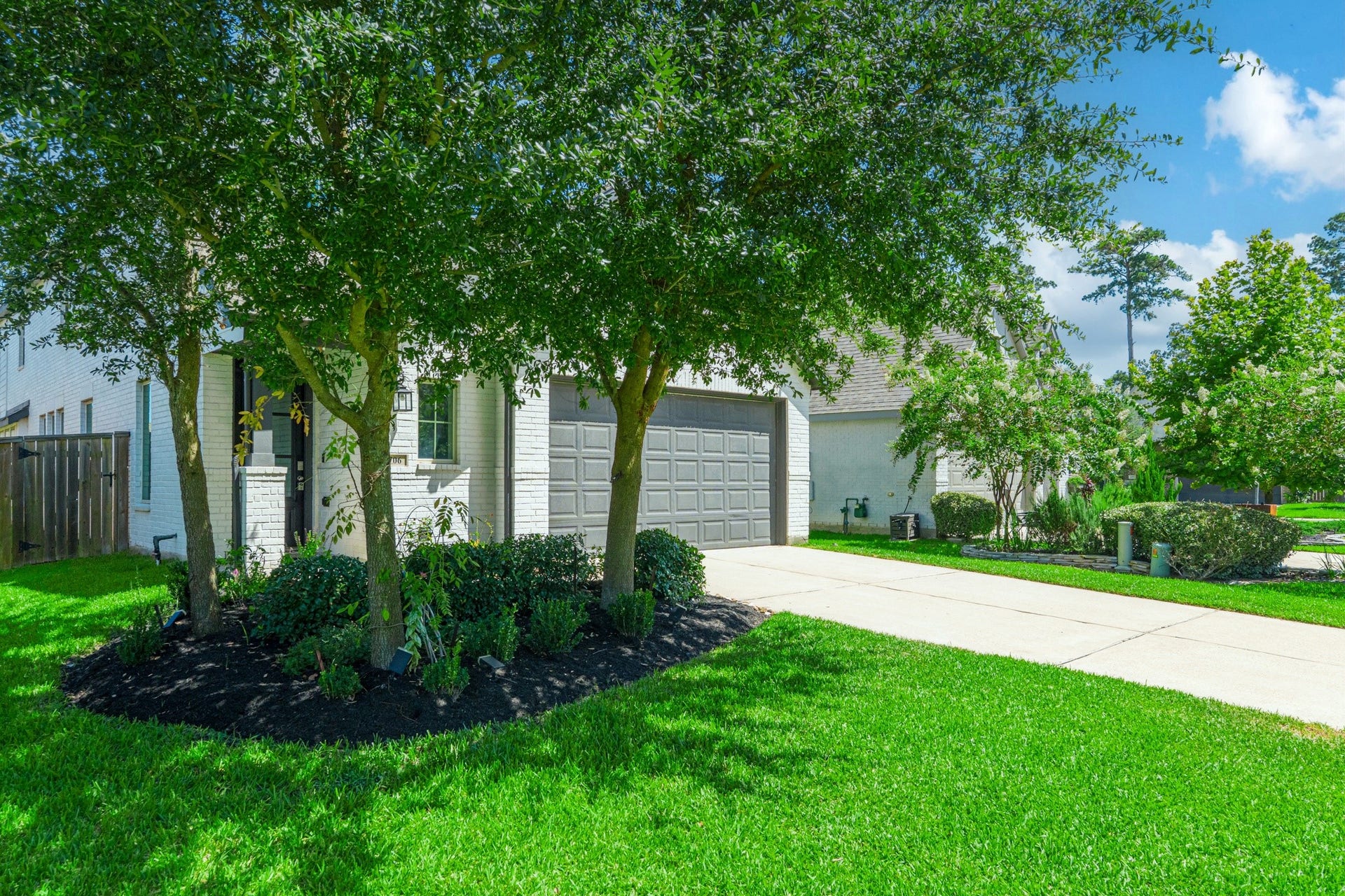 706 Santa Elena Trail, Conroe, TX 77304 Street-level front view highlighting the home's mature trees, lush green landscaping, and wide concrete driveway leading to the attached two-car garage. This home's exterior is both welcoming and unmistakably modern a true standout in the neighborhood.