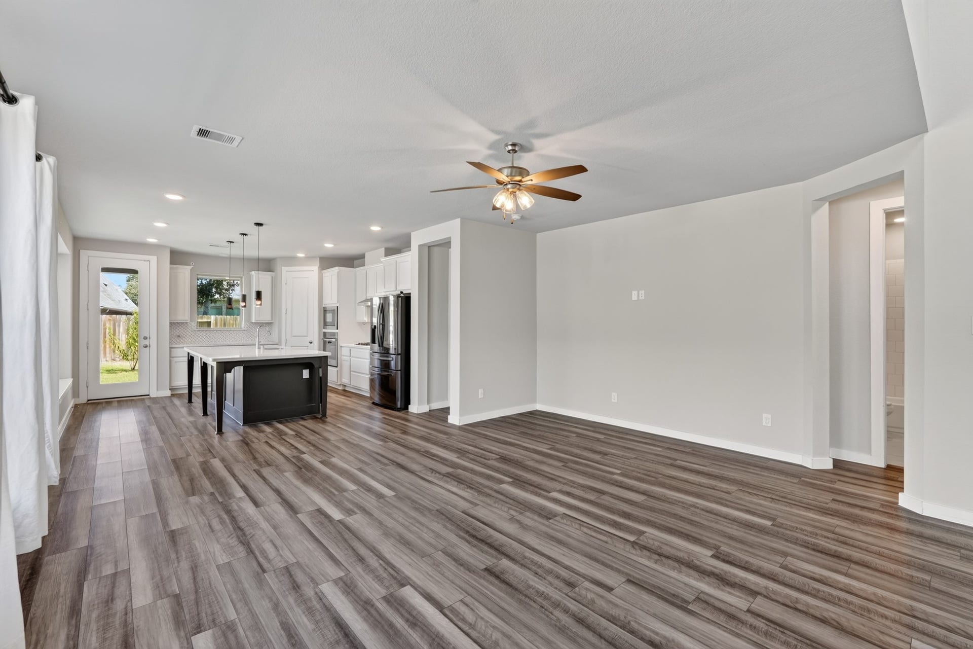706 Santa Elena Trail, Conroe, TX 77304 Another angle of the open and airy family room showcases the ceiling fan, dark hardwood flooring, and the seamless open connection to the kitchen and dining areas beyond. This floor plan was designed for real life and it shows beautifully in every view.