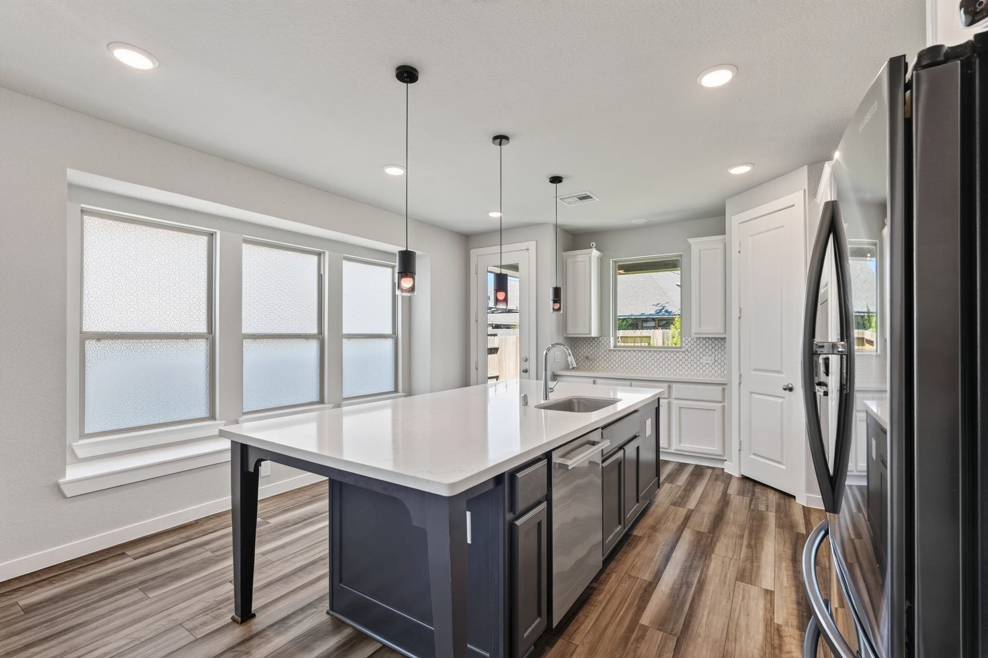 706 Santa Elena Trail, Conroe, TX 77304 Natural light pours in through the kitchen window, illuminating the white quartz island, stainless appliances, and the open layout beyond. The view from here perfectly captures the home's seamless and beautifully designed open-concept floor plan.