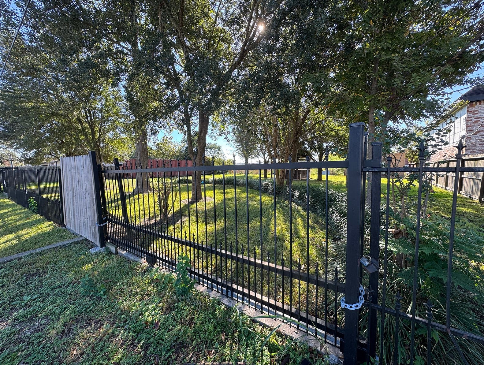 This photo shows a spacious, grassy yard with mature trees, enclosed by a sturdy metal fence with gate, providing a private and serene outdoor space.
