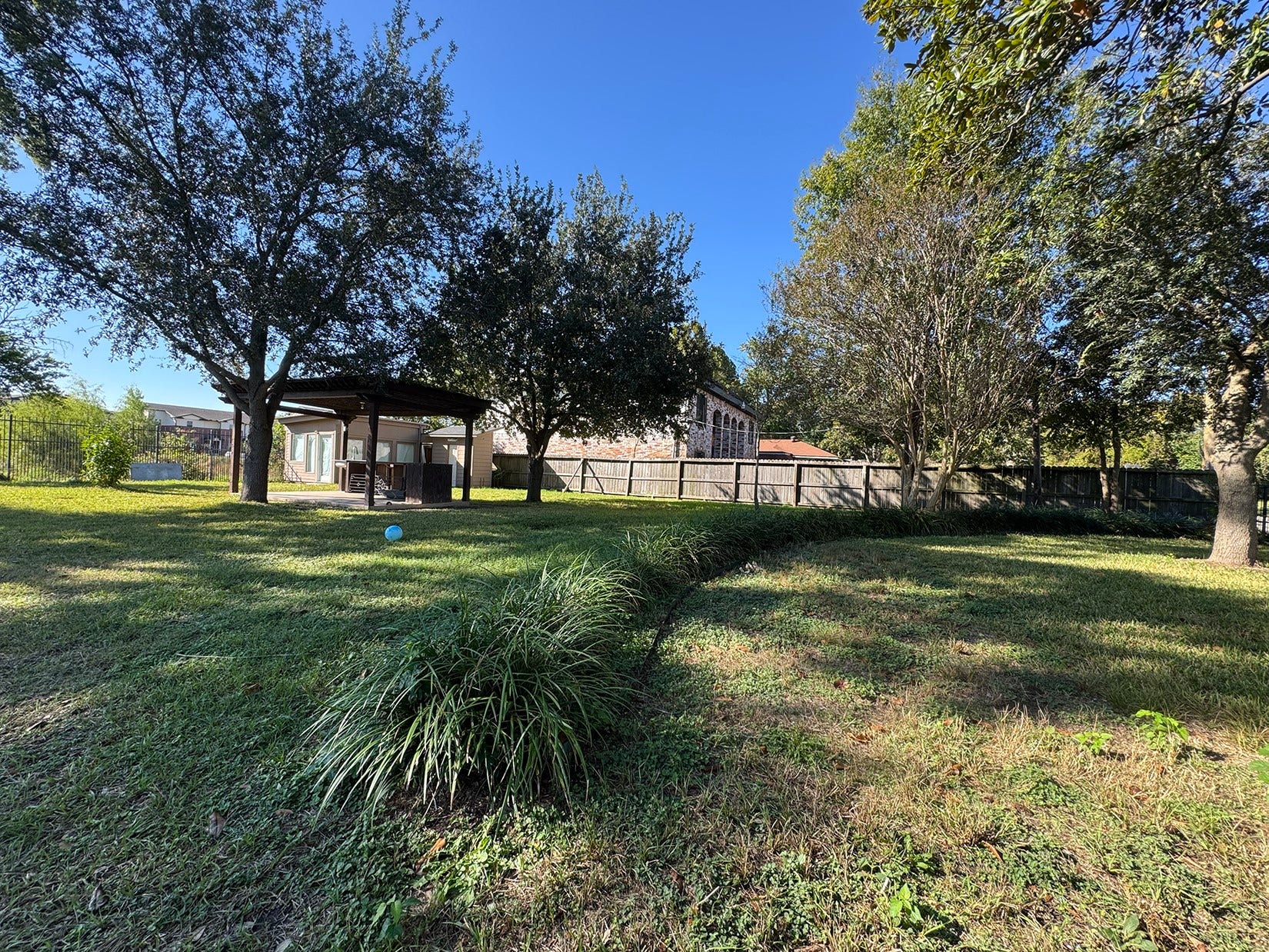 Spacious yard with well-maintained grass, mature trees providing shade, and a wooden deck area. Perfect for outdoor activities and relaxation.