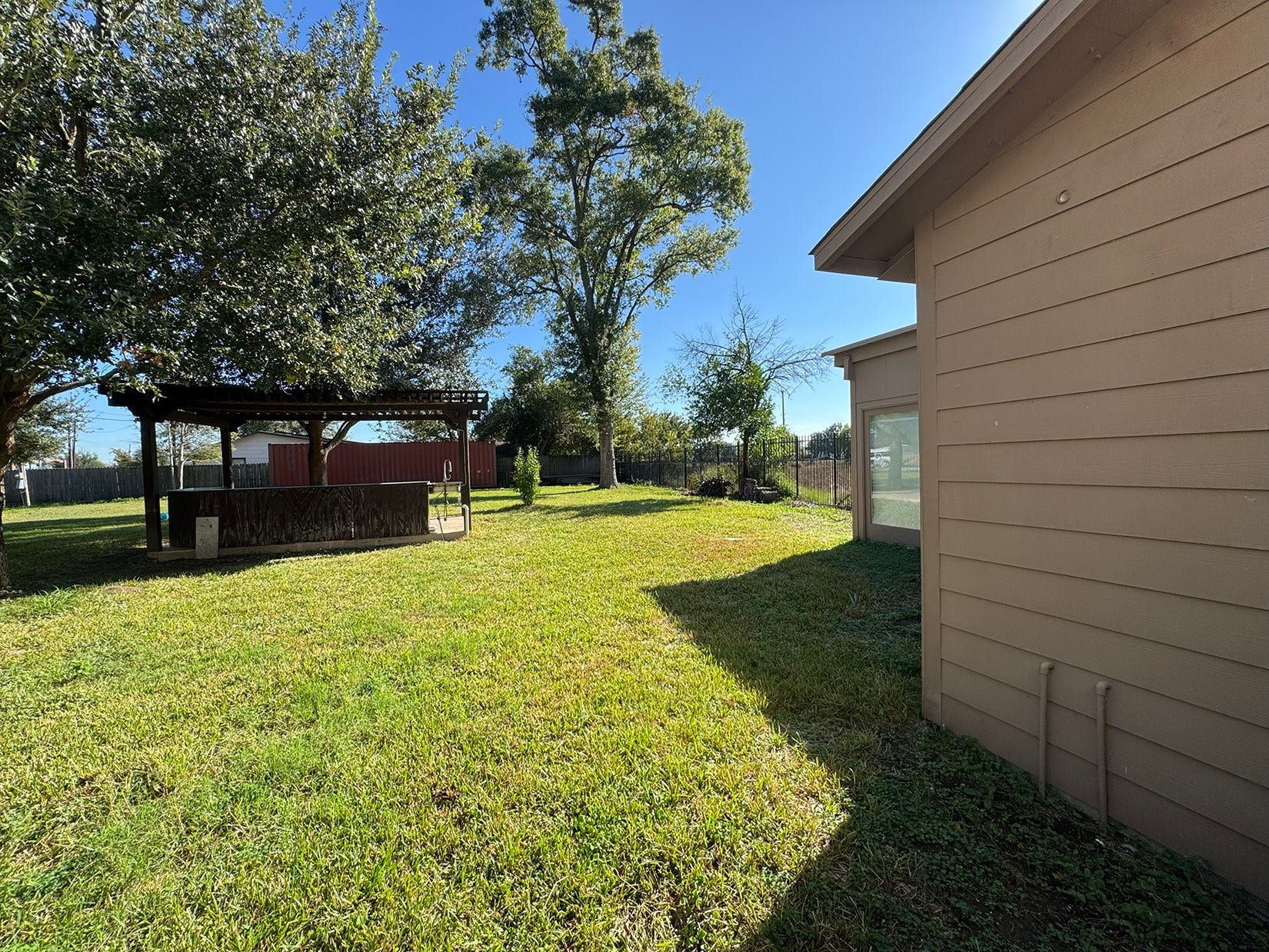 Spacious backyard with a well-maintained lawn, featuring a wooden pergola perfect for outdoor gatherings. Mature trees provide shade and privacy.