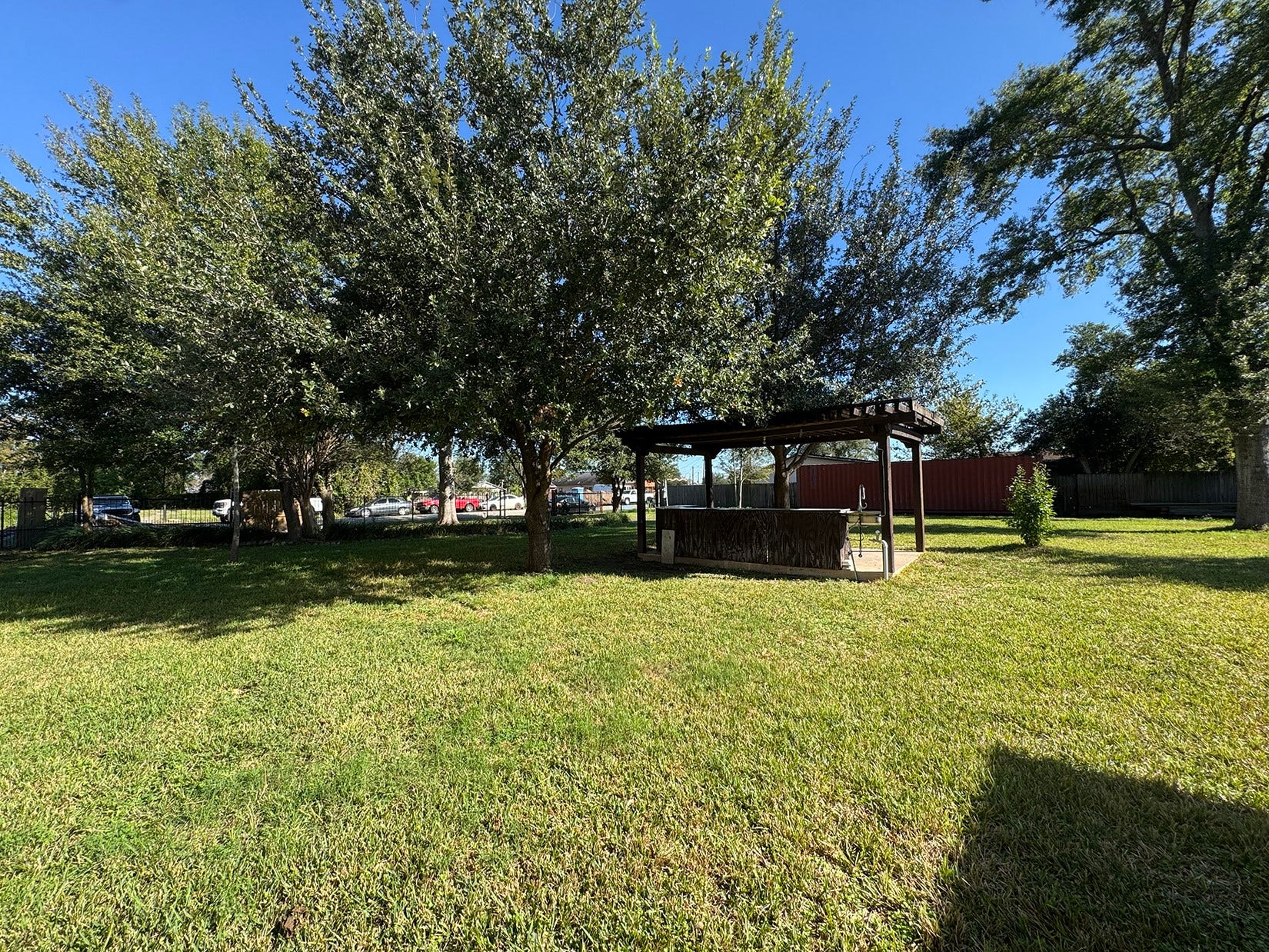 The photo showcases a spacious backyard with lush grass, mature trees providing ample shade, and a wooden gazebo, perfect for outdoor relaxation or entertaining.