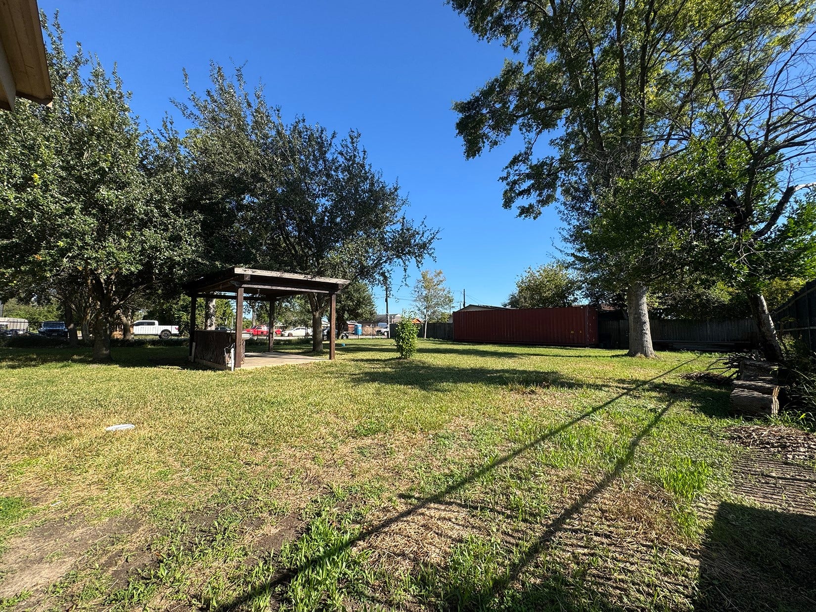 Spacious backyard with lush grass, mature trees, and a wooden pergola, perfect for outdoor gatherings and relaxation.