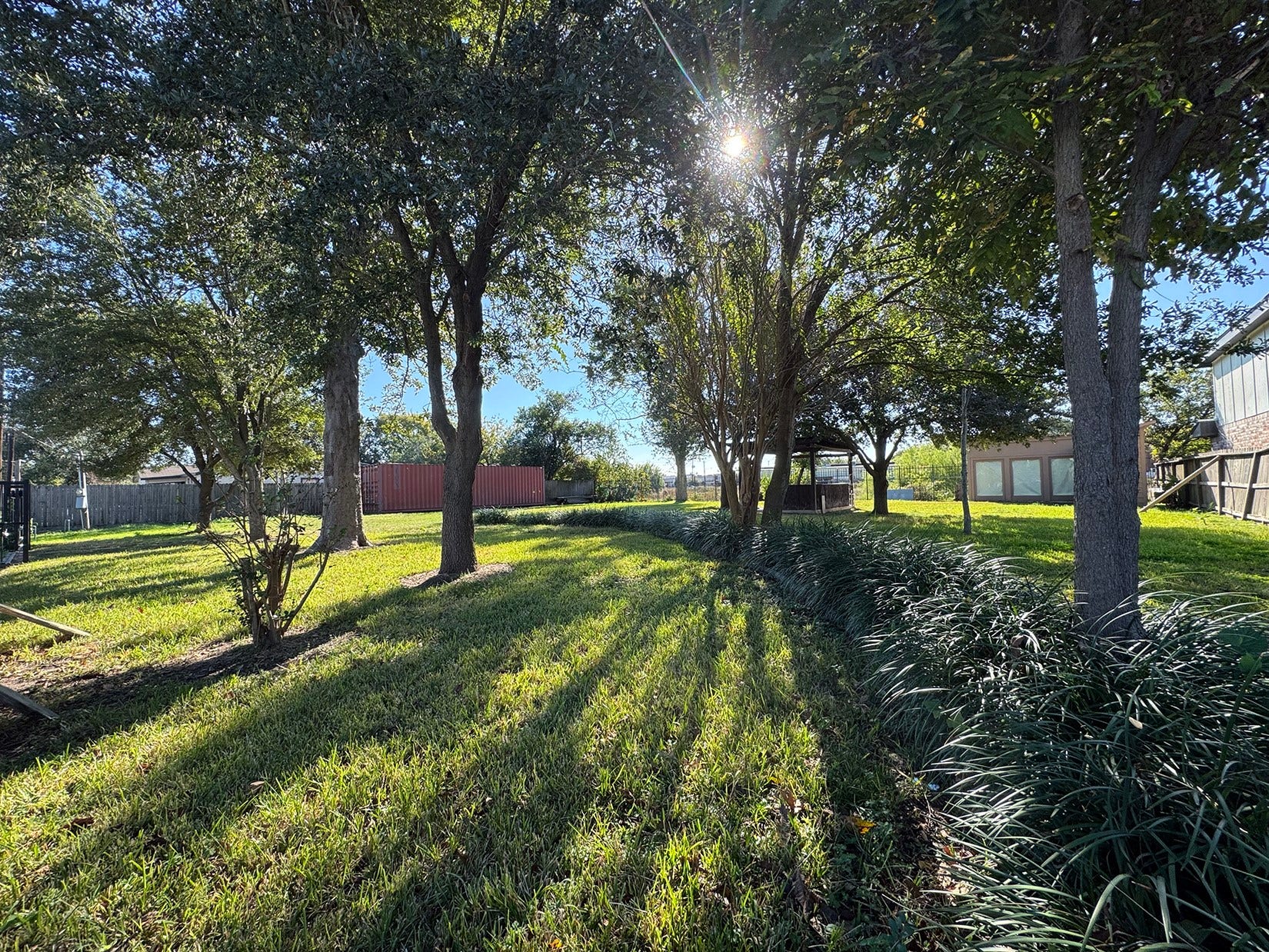 This photo showcases a spacious, sunlit backyard with mature trees providing ample shade, a well-maintained lawn, and a fence for privacy. Ideal for outdoor relaxation and activities.