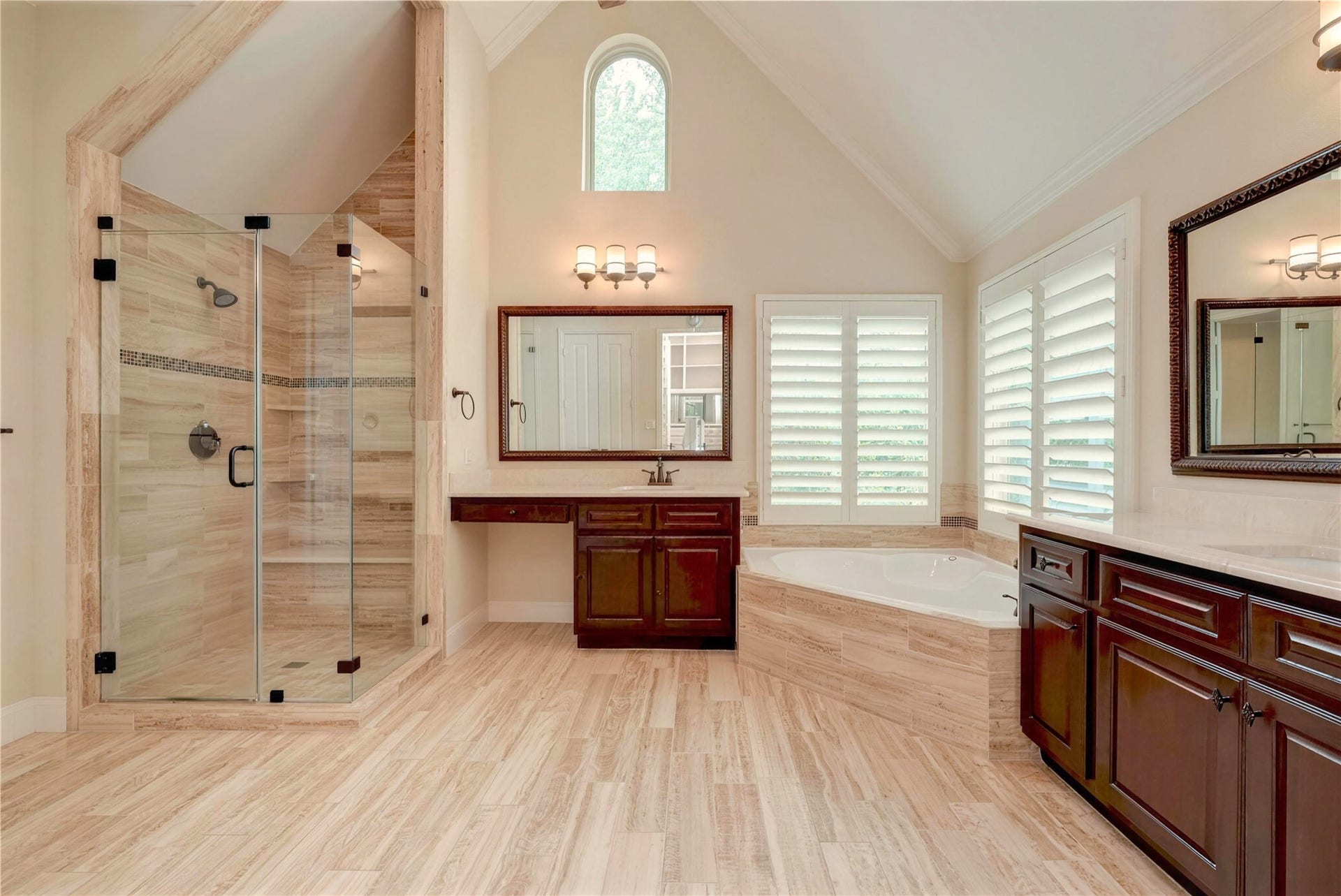 19 Herons Flight Place, Spring, TX 77389 Luxurious bathroom featuring a spacious glass-enclosed shower, elegant soaking tub, and rich wood cabinetry, all illuminated by natural light from a high, arched window.
