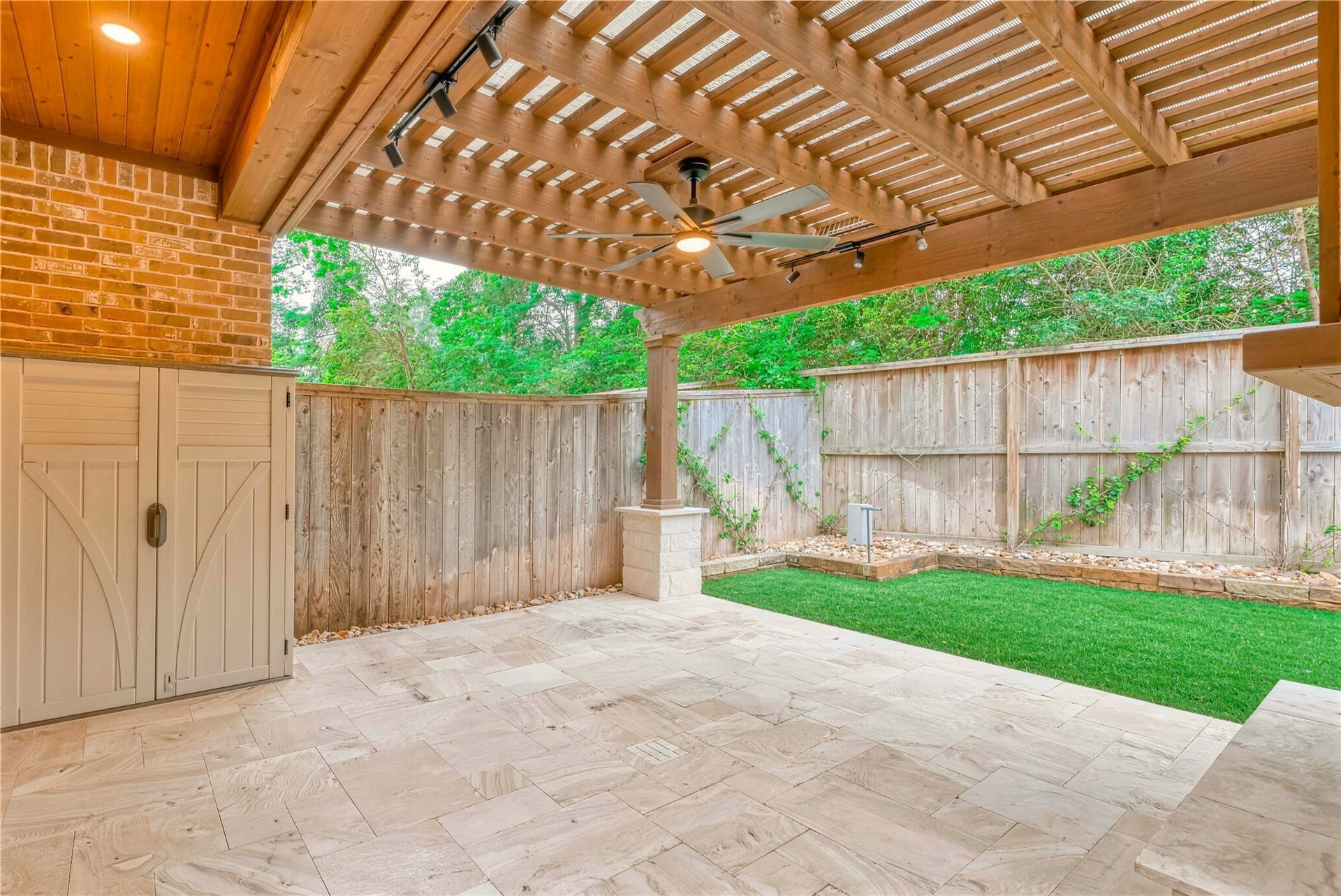 19 Herons Flight Place, Spring, TX 77389 Charming patio with a wooden pergola, ceiling fan, and elegant stone flooring, ideal for outdoor relaxation. The fenced yard offers privacy and a touch of greenery.