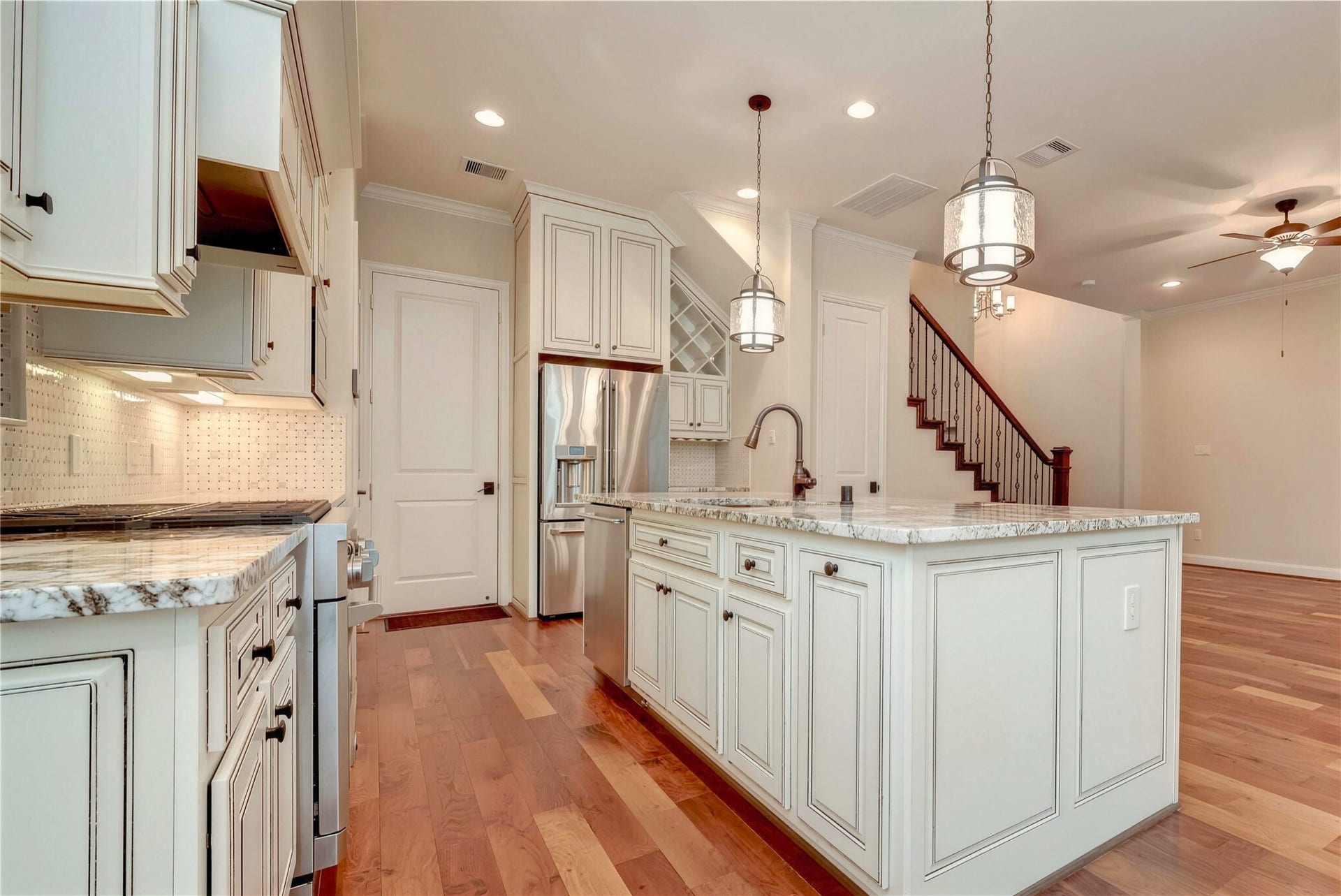 19 Herons Flight Place, Spring, TX 77389 Elegant kitchen featuring granite countertops, stainless steel appliances, and pendant lighting, seamlessly connecting to a living area with hardwood floors and a stylish staircase.