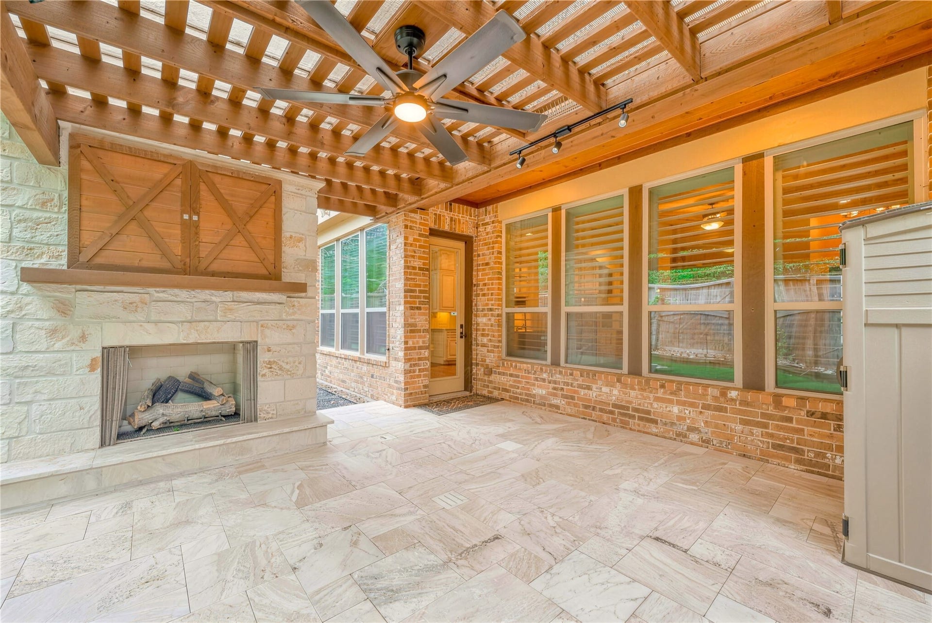 19 Herons Flight Place, Spring, TX 77389 Charming outdoor living space featuring a cozy stone fireplace, sleek ceiling fan, and elegant pergola, perfect for relaxing or entertaining guests.